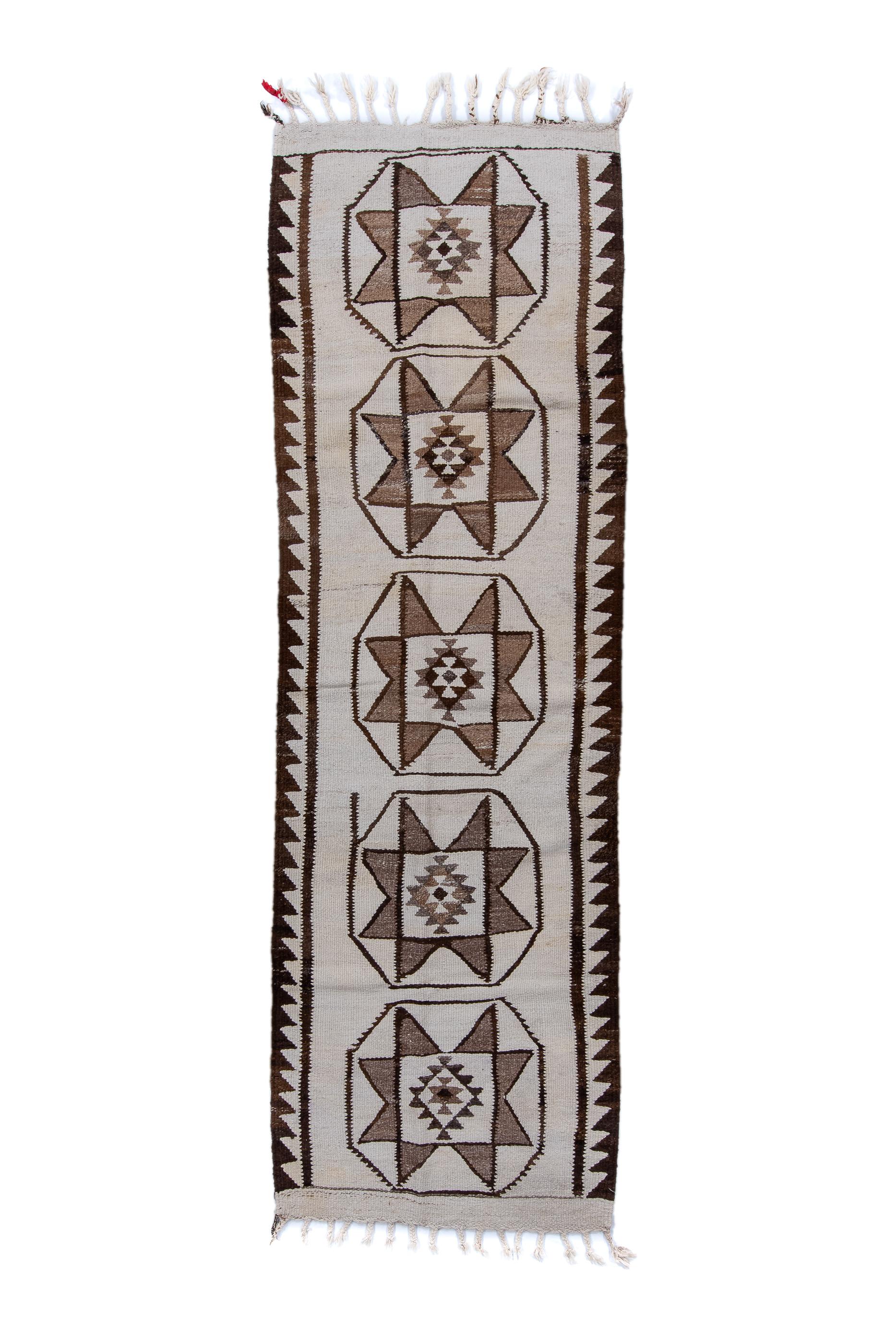 The cream field displays five floating octagons enclosing each an eight pointed star, with details in red and  brown. Sawtooth bitonal side borders. No end borders but cream flatweave finishes with tassels. Slit tapestry weave with wool pattern
