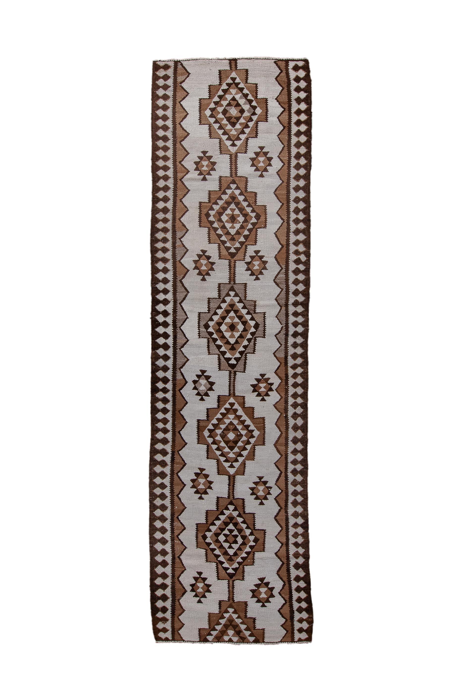 This wool weft faced, slit tapestry technique kenare (runner) displays an ecru field centred by a pole medallion of five and a half stepped and nested lozenges, detailed in coral and ecru. Small, upright ashik secondaries. Inner triangle band and a