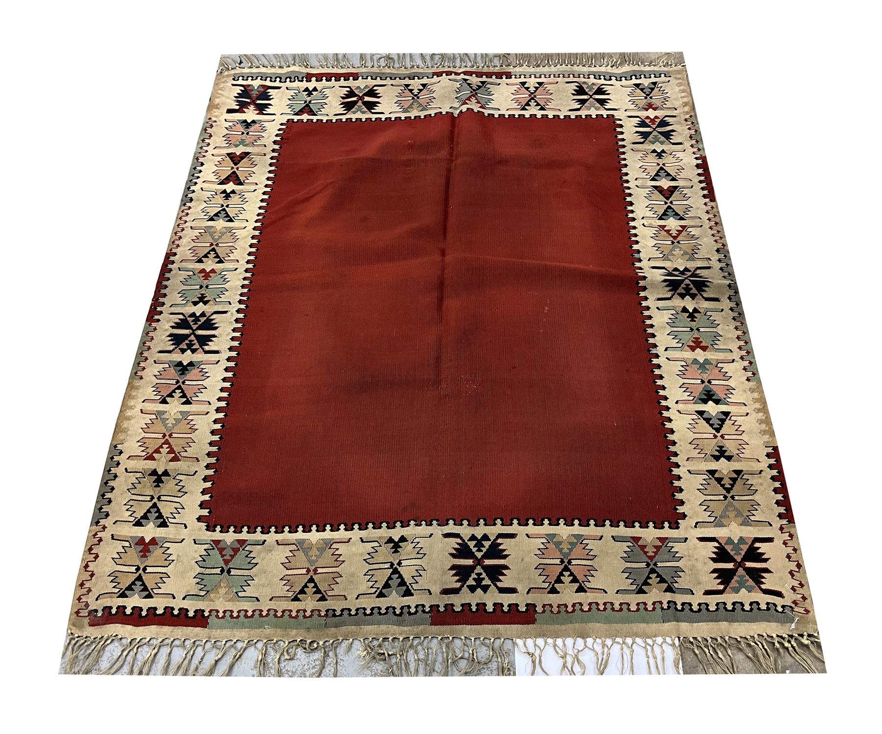 This flatwoven kilim area rug is an excellent example of kilim rugs woven in the 1920s in Anatolia, Turkey. The design is simple yet eye-catching. They featured a maroon red open field framed by a repeating pattern cream border woven with pink,
