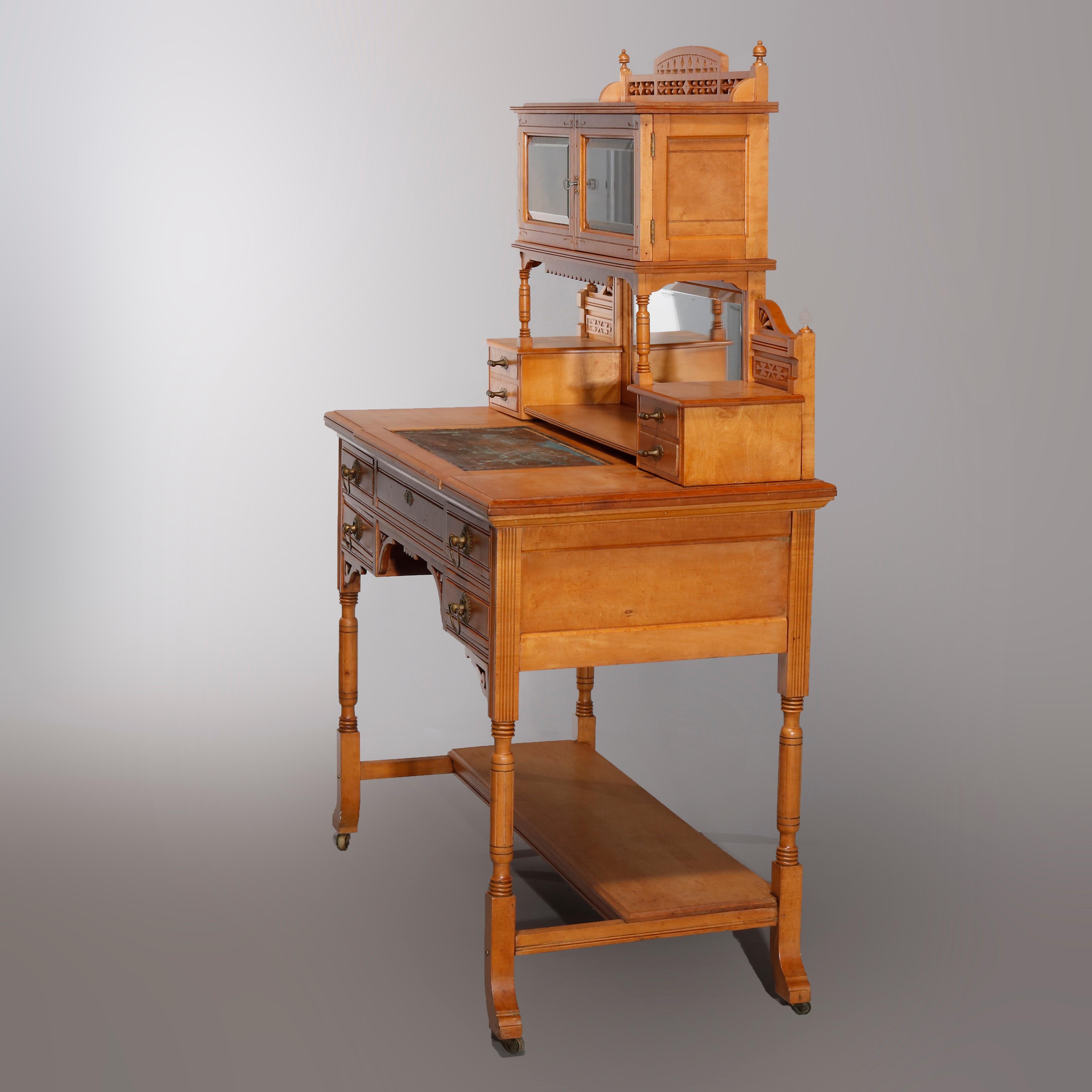 An antique Aesthetic Movement ladies desk in the manner of Kimble & Camus offers birdseye maple construction with upper double glass door cabinet having pierced gallery over mirrored backsplash with flanking small drawers, writing surface is slide