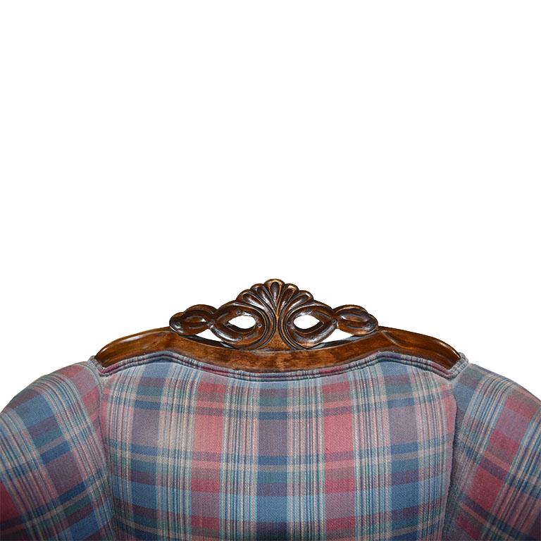A beautiful pair of antique carved wood chairs with rolled arms and plaid upholstered seats. This set features carved wood bases with stylized backs and bases. One of the chairs is larger, the 