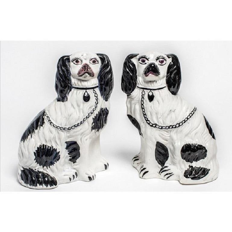 Handsome pair of porcelain black and white Staffordshire Dogs, made in England at the turn of the century. Due to its handpainted nature, each dog figurine has a distinct face with expressive eyes and muzzle. The seated dogs sport matching black