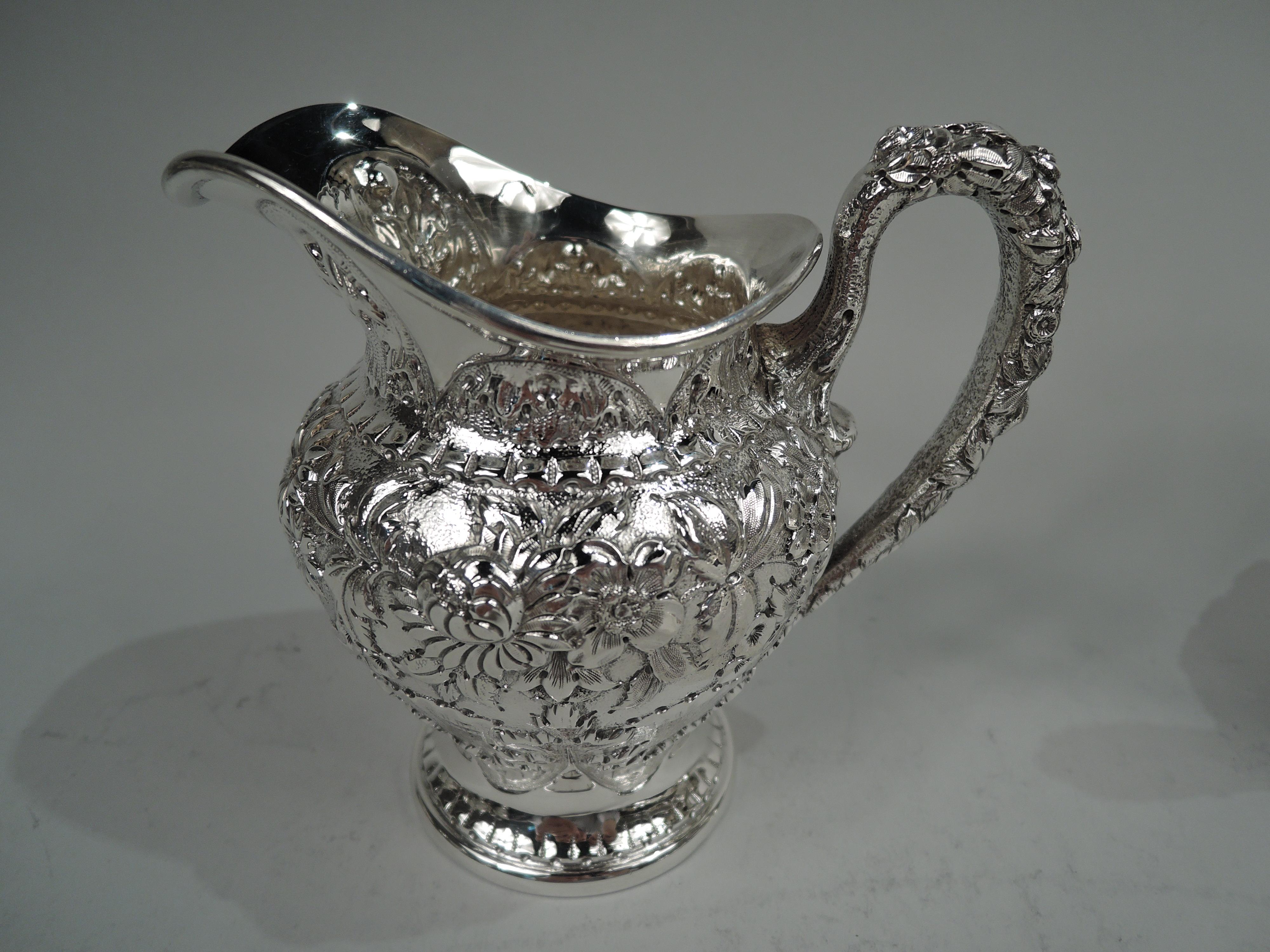 Pair of Edwardian sterling silver creamer and sugar. Made by S. Kirk & Son Inc. in Baltimore. Ovoid bodies and high looping handles. Creamer has helmet mouth and sugar has raised cover and finial. Frond and flower repousse; at bottom leaf and