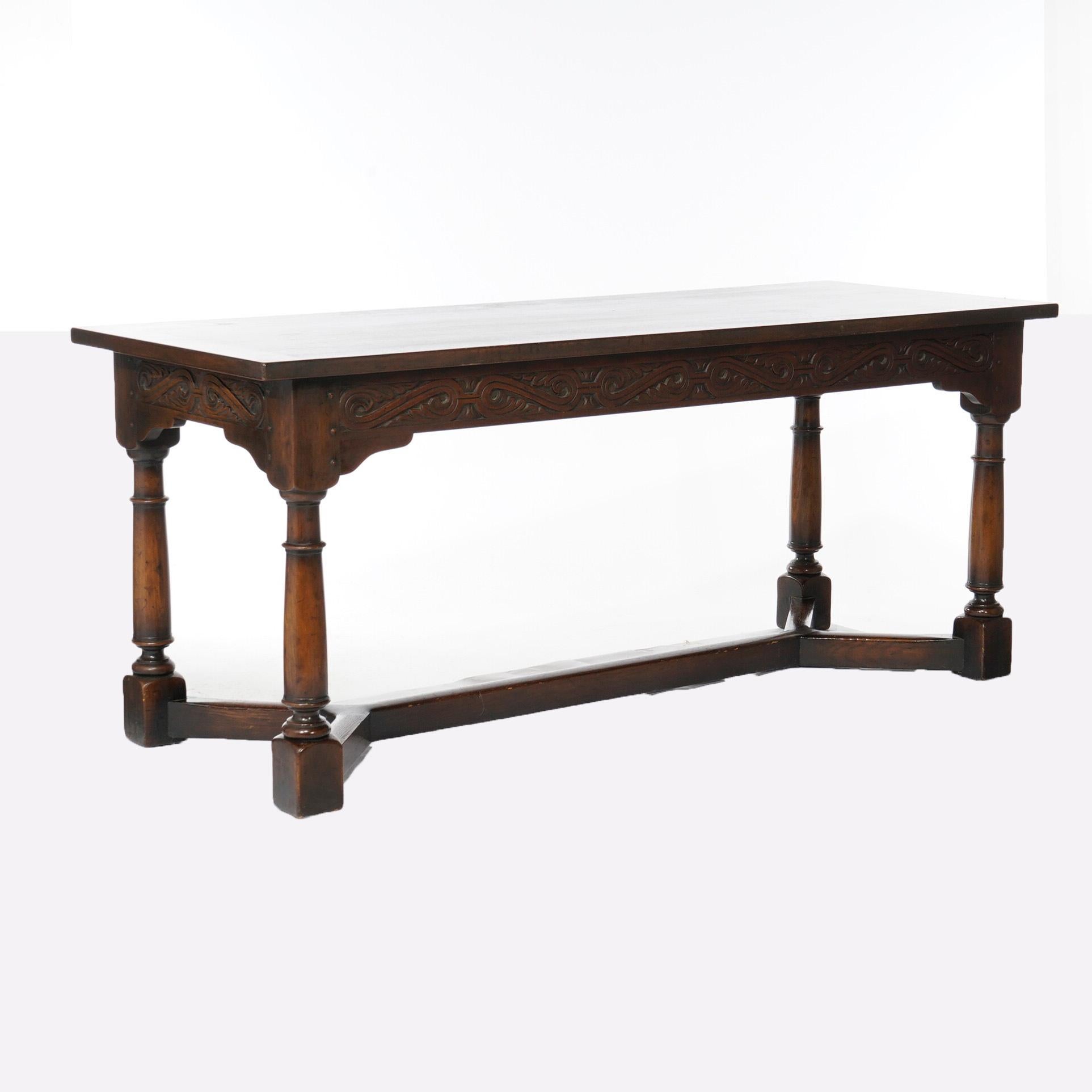 AN antique long sofa table by Kittinger offers oak construction with deeply carved skirt having scroll and foliate design, raised on balustrade legs with cross stretcher as photographed, c1910

Measures- 30.25''H x 72''W x 27''D.
