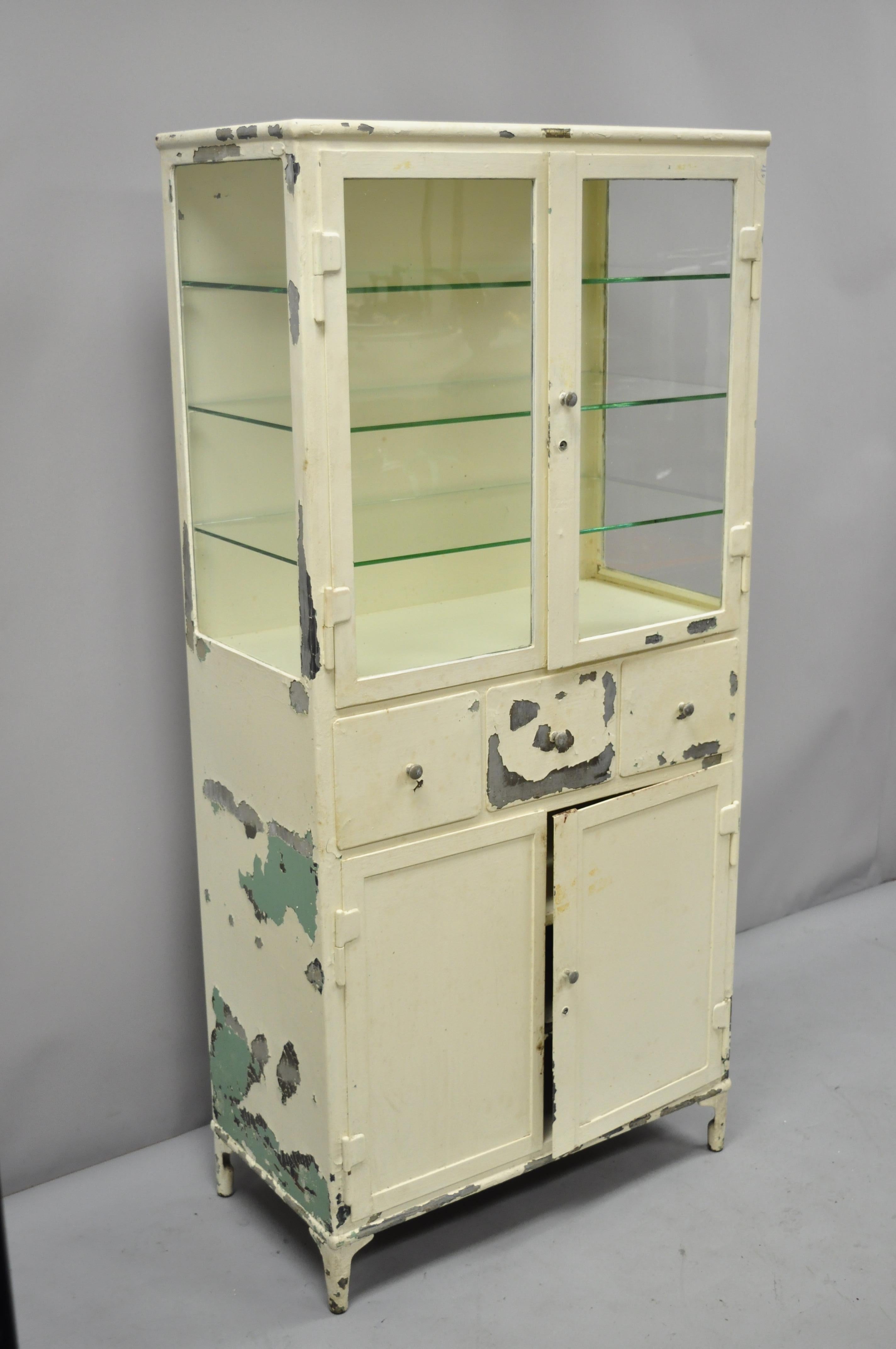 Antique Kny Scheerer steel metal glass medical dental pharmacy cabinet. Item features glass sides, metal frame, 4 swing doors, original tag, no key but unlocked, 3 drawers, 3 glass shelves, circa early 1900s. Measurements: 64.5