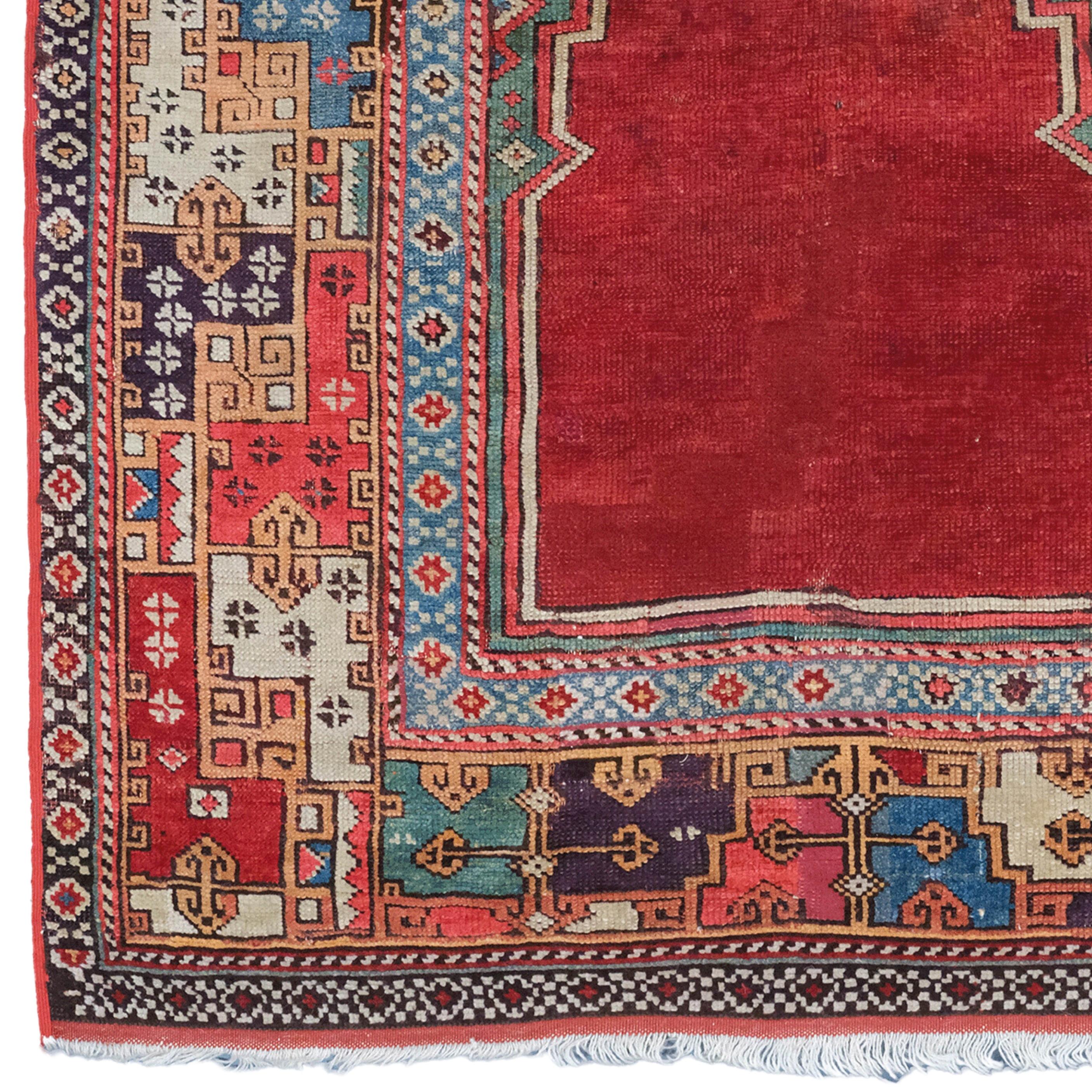 This antique carpet is an Anatolian Konya carpet from the 19th century. There is a red, mihrab-shaped pattern in the center of the carpet, which suggests that the carpet was used for worship purposes. There are geometric motifs in green and blue