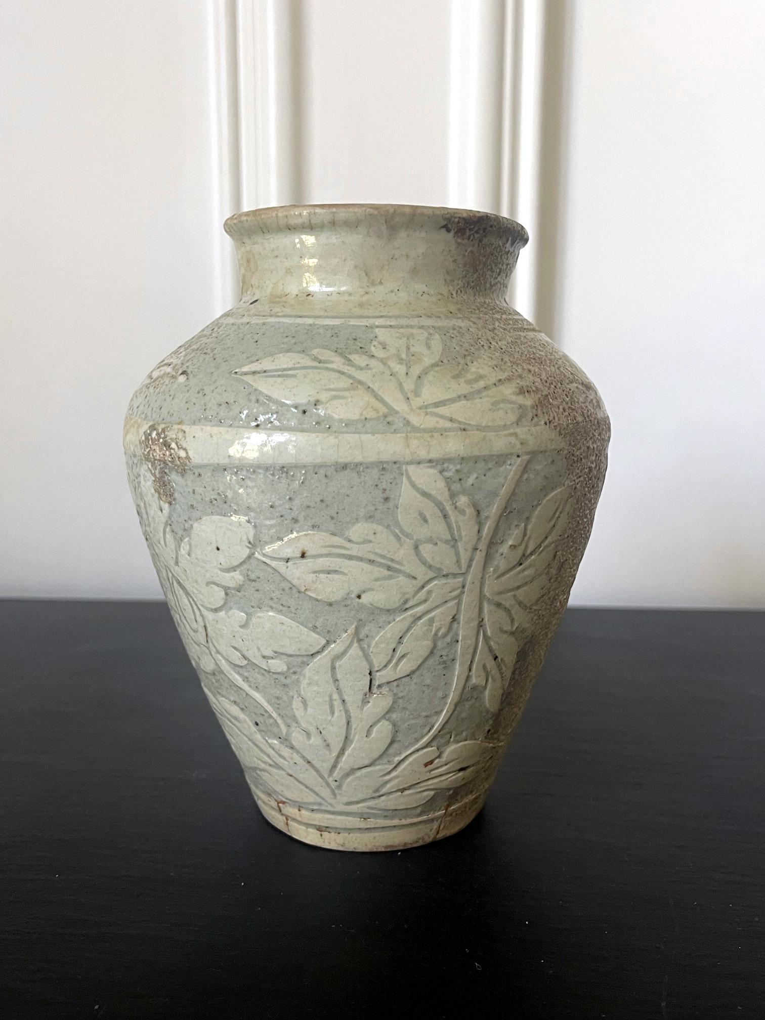 A Korean ceramic bottle form jar of Buncheong ware circa 15-16th century Joseon Dynasty. The surface of the jar features a celadon glaze and an elaborate incised design of large floral and leaves, possibly representing peony. Particularly, one side