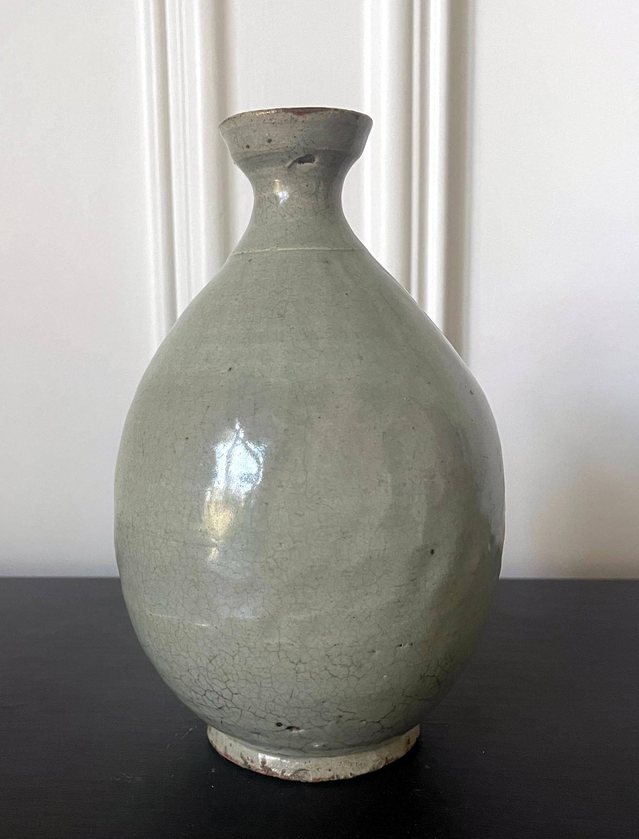 A Korean ceramic bottle-form vase circa 16th century Joseon Dynasty. It was likely intended as a wine bottle, the pear-shaped vessel with flaring neck feature a celadon glaze exterior with subtle incised patterns around the neck and mid-body.