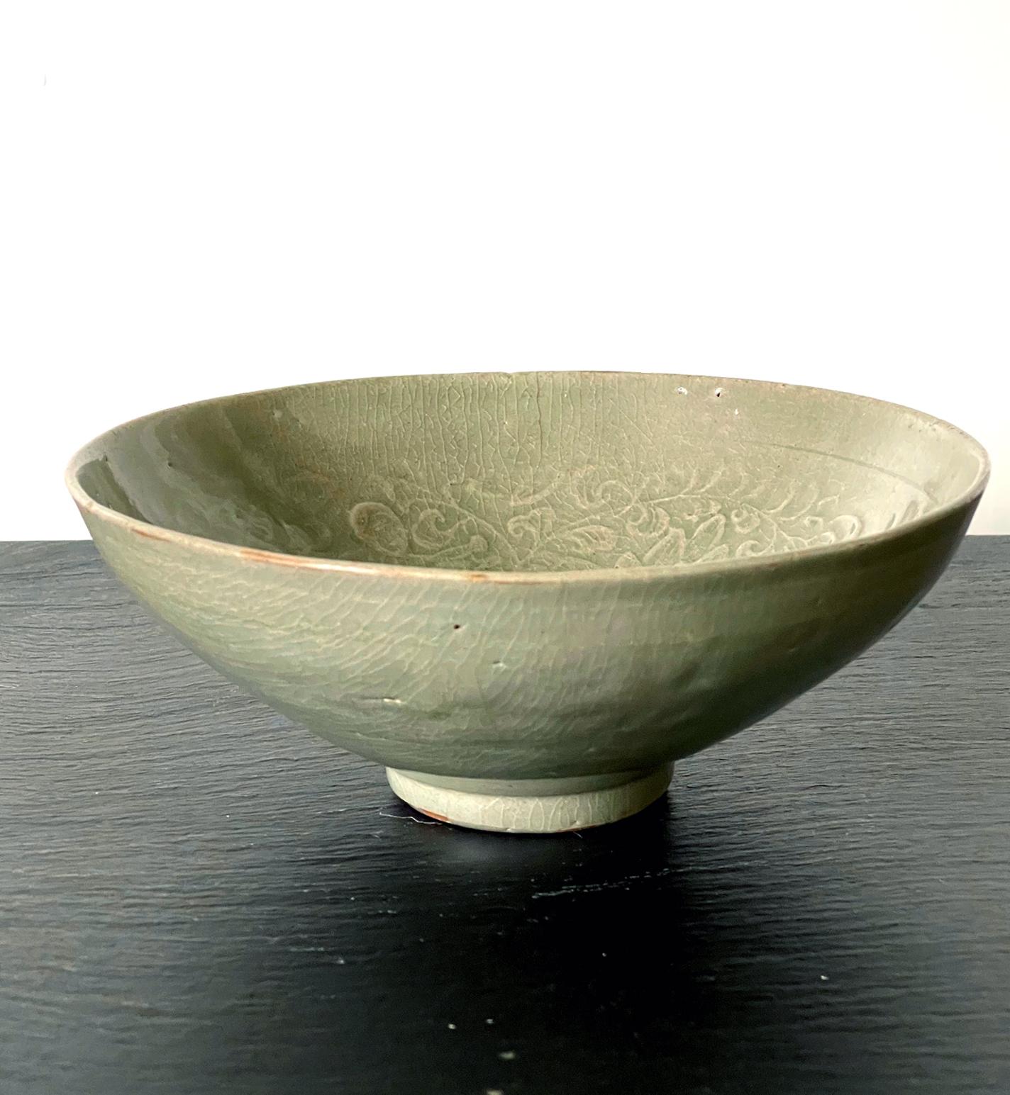A Korean stoneware bowl from Goryeo dynasty circa 12th century. The conical form bowl with a small raised foot rim is covered in a celadon green glaze. Under the glaze, the interior is decorated with carved design of bands of scrolling foliage with