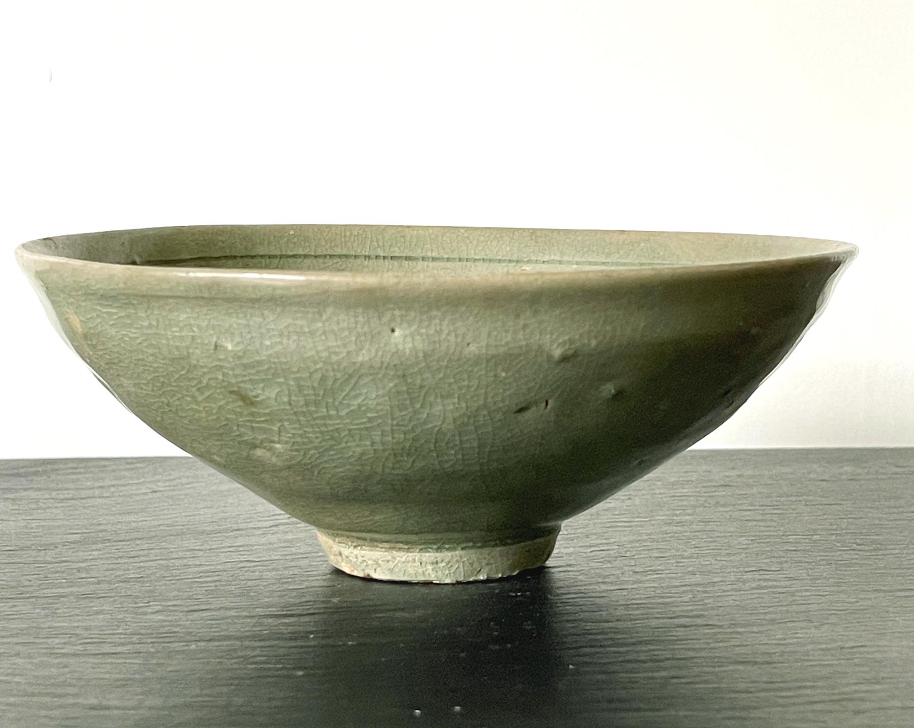 A Korean stoneware bowl from Goryeo dynasty circa 12th century. The conical form bowl with a small raised foot rim is covered in a celadon green glaze. Under the glaze, the interior is decorated with carved design of a floral pattern with scrolling