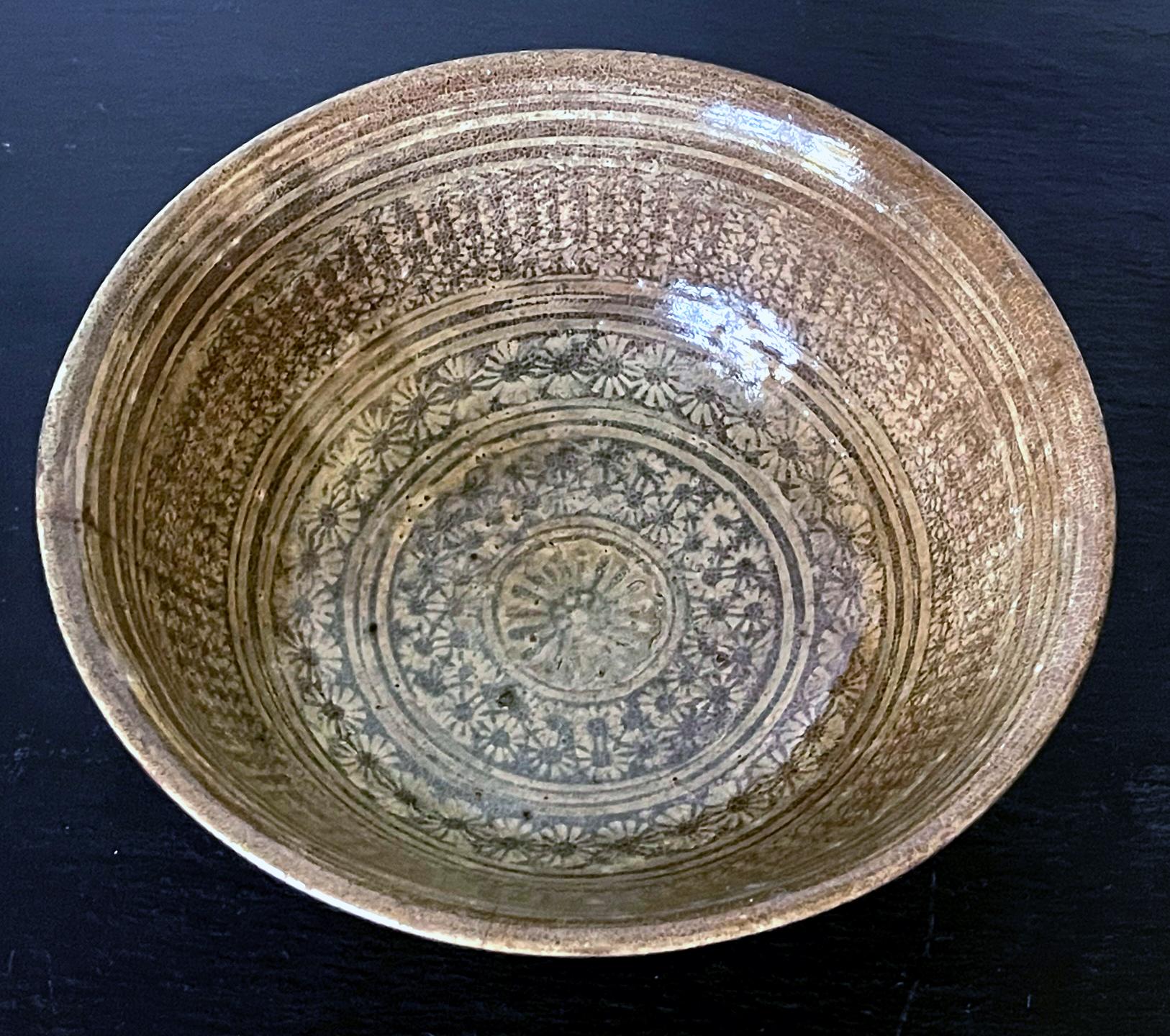 A Korean ceramic bowl supported on a short ring foot in the classic Buncheong (or Punch'ong) style from early Joseon Dynasty circa 15th century. The bowl features a beautiful dense composition of white slip decoration using stamping technique. With