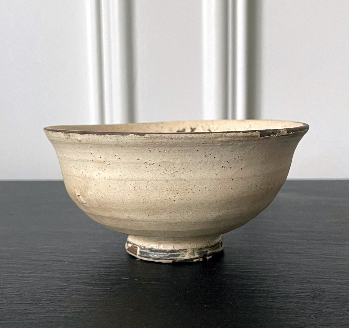 A ceramic tea bowl with milky white glaze made in Korea for Japanese market circa 16-17th century. 
The thinly potted bowl is in the shape called Hatazori-gata (curving-lip type) that is known as Komogai (or Kumagawa) type. It was named after the