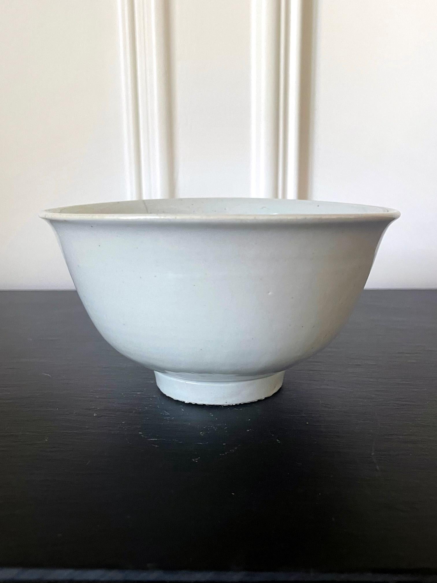 A Korean ceramic bowl covered in a white glaze with a hint of bluish green circa 18th-19th century, later Joseon Dynasty. The deep bowl features a classic form, simple but elegant with everted rim and cylindrical foot ring. The glaze was evenly