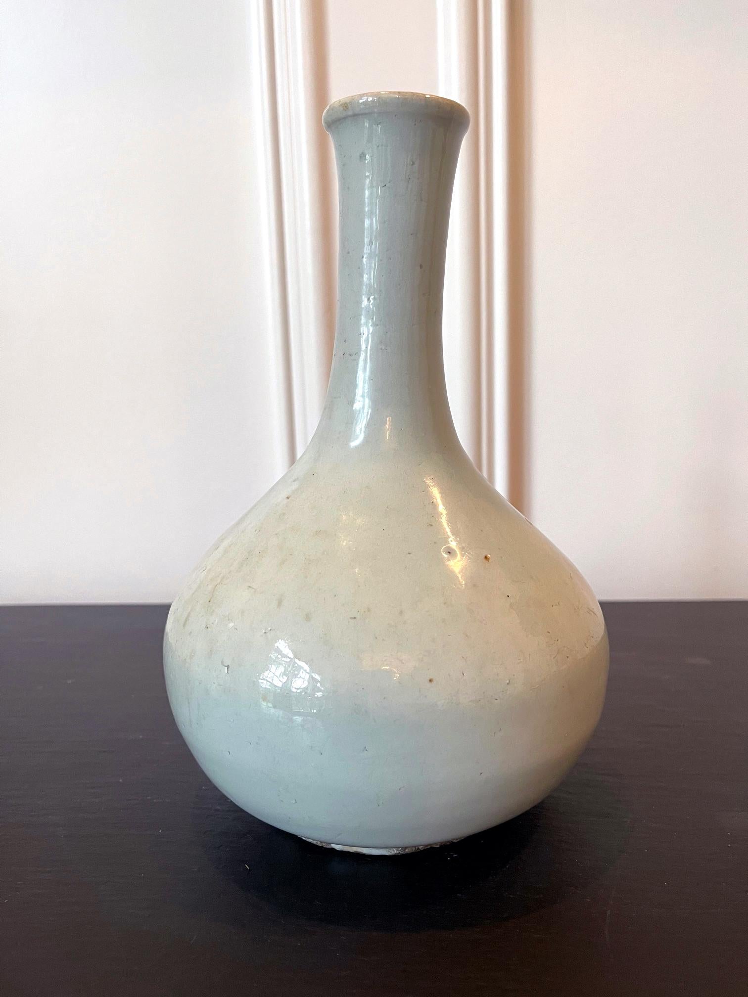 A Korean ceramic bottle vase circa 19th century late Joseon Dynasty (1392-1910). The vase is of a classic bottle form with a bulbous body and a long neck with a slightly rolled mouth rum. The glaze is mostly white with a slight blueish tint, but in