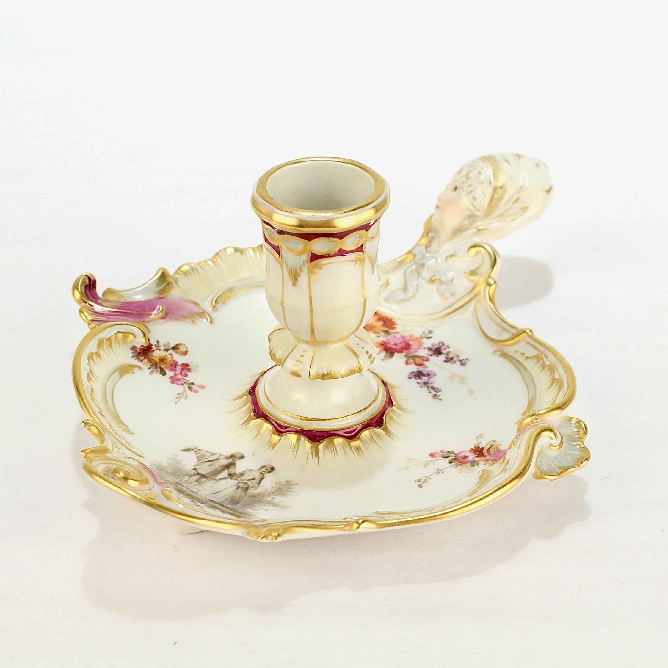 A fine antique figural porcelain candlestick or chamberstick.

By KPM Royal Berlin.

The handle is a figural maiden's head with gilt highlights. The gilding continues around the entirety of the wax pan, which is further decorated with pink, purple,