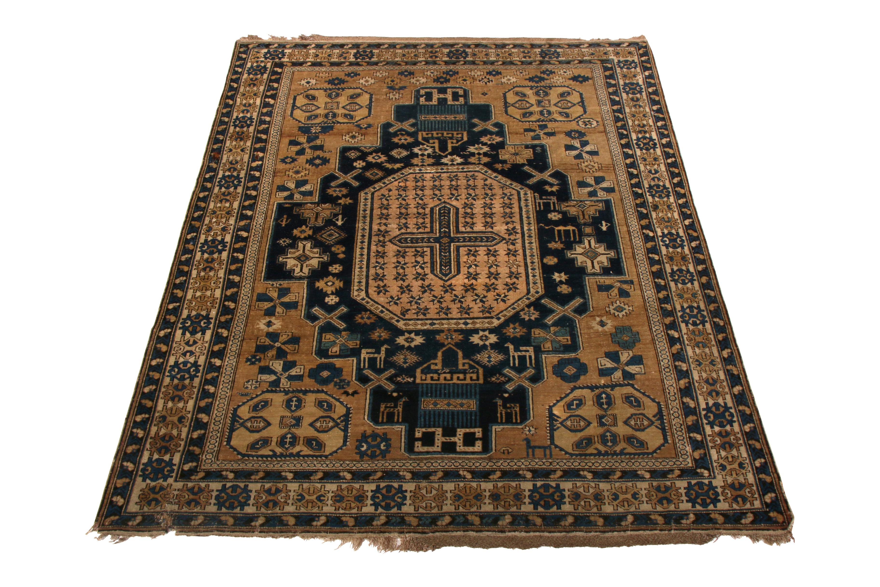 Hand knotted in wool originating from Russia between 1910-1920, this antique Kuba rug enjoys a more regal take on traditional colorway hues this time-honored rug family celebrates, a play of rich beige brown and abrashed blue bringing out the