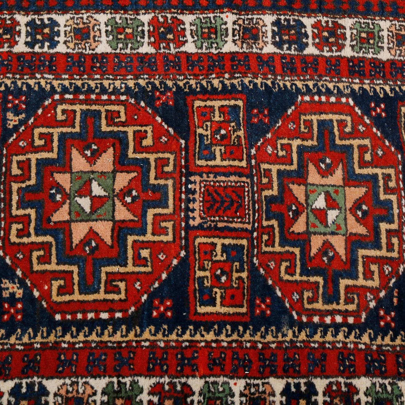 An antique Kurd Nomadic Tribal Oriental rug offers wool construction with double geometric medallions with additional geometric tribal designs on blue ground with border having repeating pattern of stylized flowers, palette includes navy, red, moss