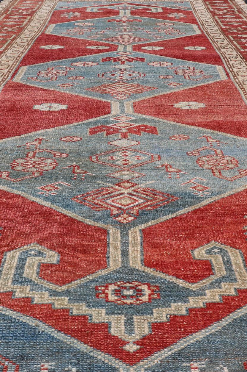 With brilliant design and vibrant colors, this Kurdish medallion-designed gallery runner features a bold burnt red, accompanied by a soft denim blue. Accent motifs of fawn and foliage are expressed in a rich cream color, giving the border and field