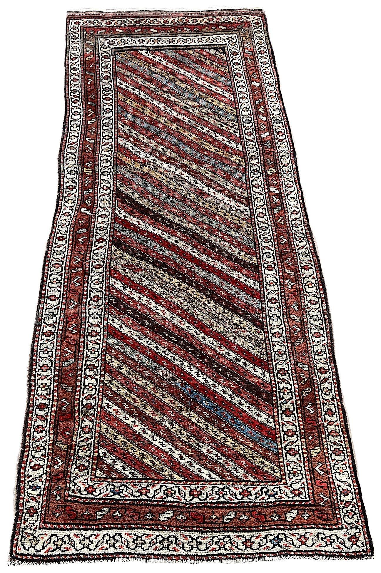 A beautiful antique Kurdish runner, hand woven circa 1900. The design features a series of multicoloured diagonal bands surrounded by a border of stylised flowers and vines. Woven with soft, velvety wool and lovely secondary colours of reds, greens,
