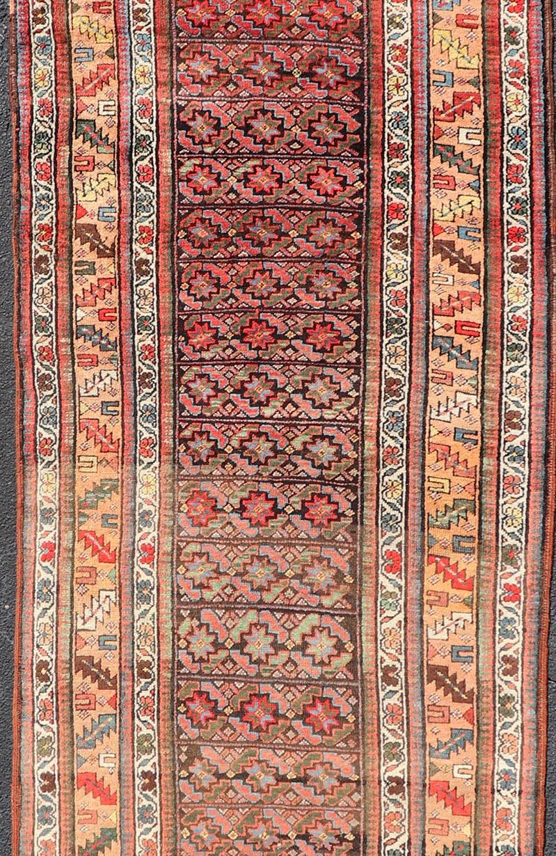 This antique runner from Persia features geometric tribal star motifs in a blue background, with accent colors of red, blue, green, and orange. The center design is tribal motifs with complimentary floral and tribal double-paneled border.