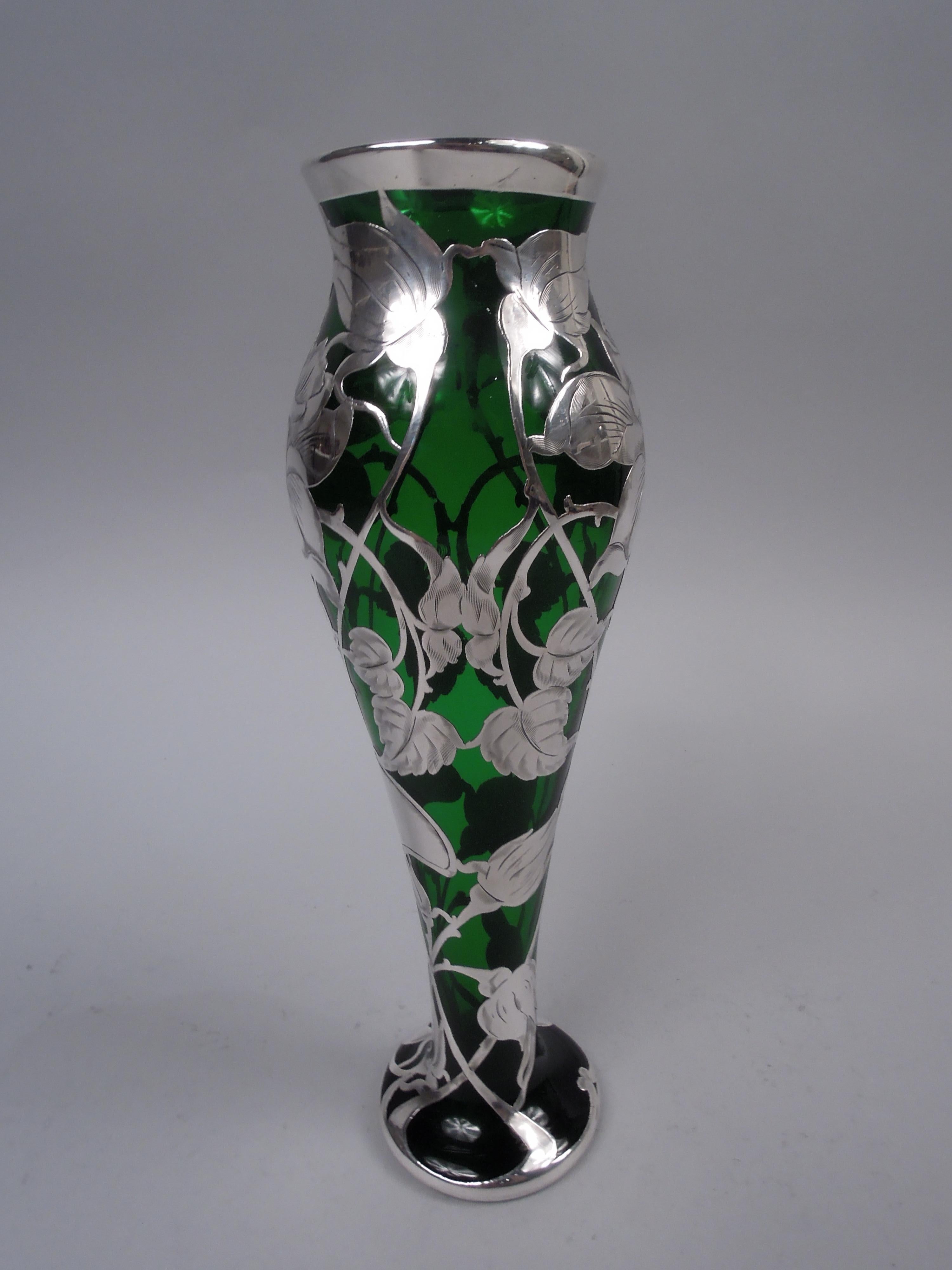Art Nouveau glass vase with engraved silver overlay, ca 1900. Baluster with gently flared mouth and round foot. Vertical overlay pattern in form of flowers with leafing and budding stems. Glass is green. Silver marked “Sterling” with La Pierre