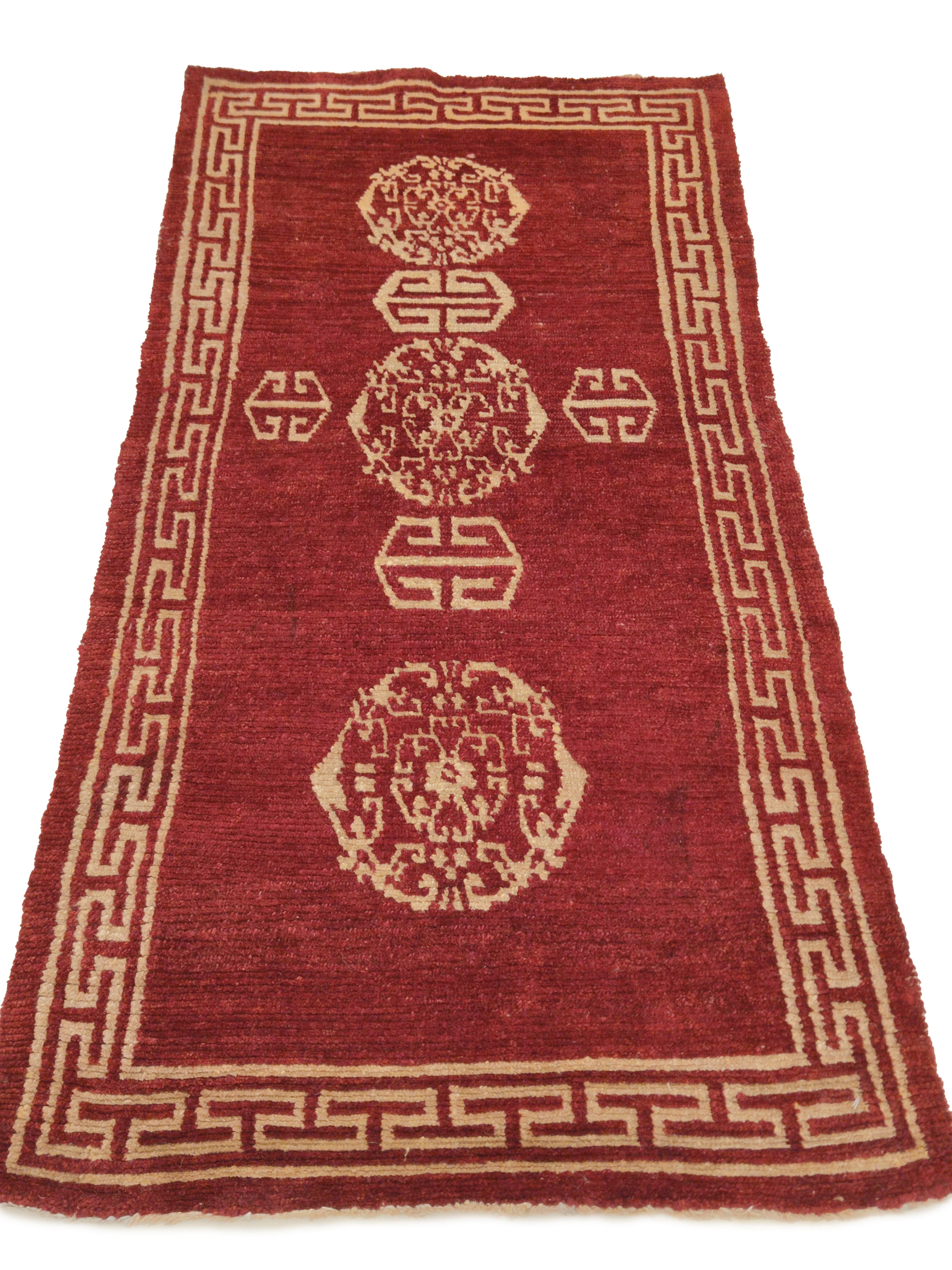 A rare Tibetan meditation rug with a lacquer red background, sparsely embellished in golden yellow by a series of lotus flower roundels alternated to geometric 'Shou' motifs, symbols of longevity. This pattern is characteristic of Chinese silk