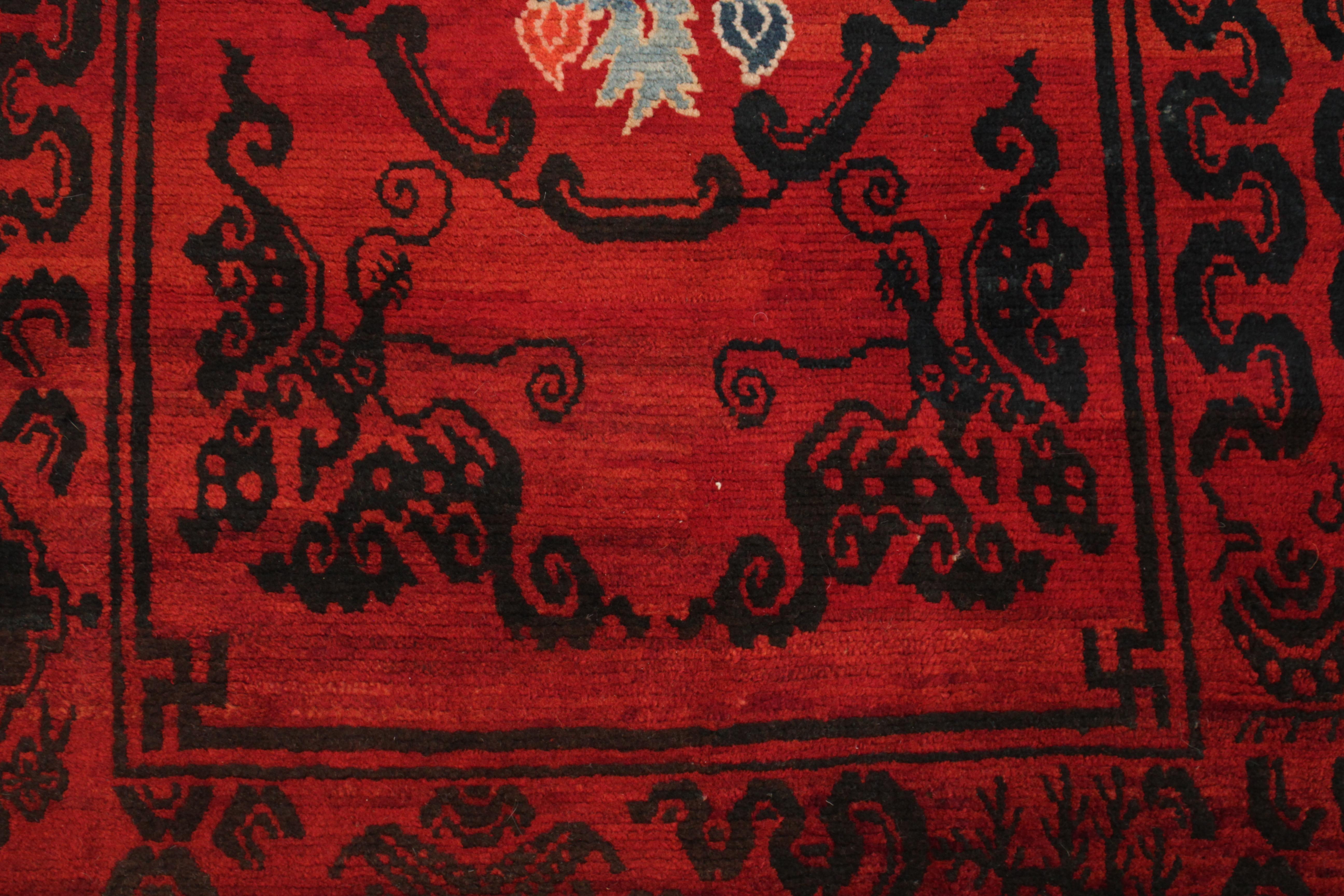 A rare Tibetan meditation rug with a lacquer red background, embellished in black and showing two bracketed roundels each containing a stylisation of the lotus flower, symbol of purity, flanked in the corners by stylised butterflies and framed by a