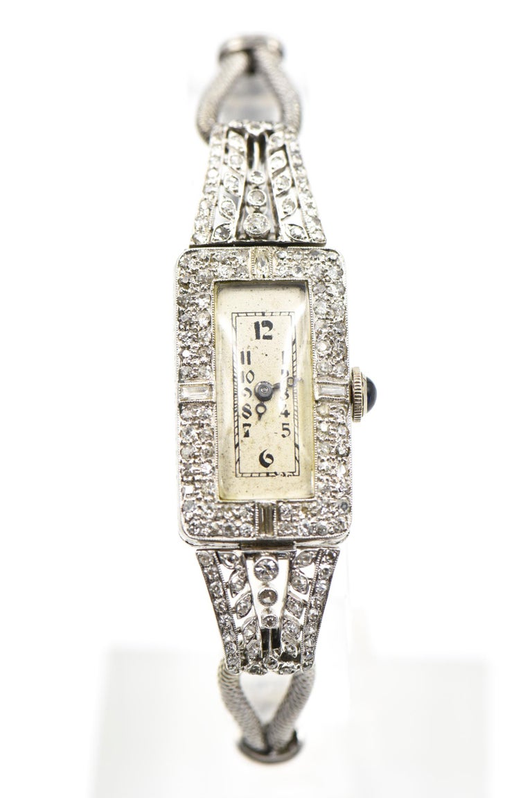 Elegant elongated platinum rectangular head with diamond frame with hinged pierced diamond garland chevron lug sides.  The band is a double woven 9k white gold design terminating with 2 bars that end with a push button clasp that also has an 