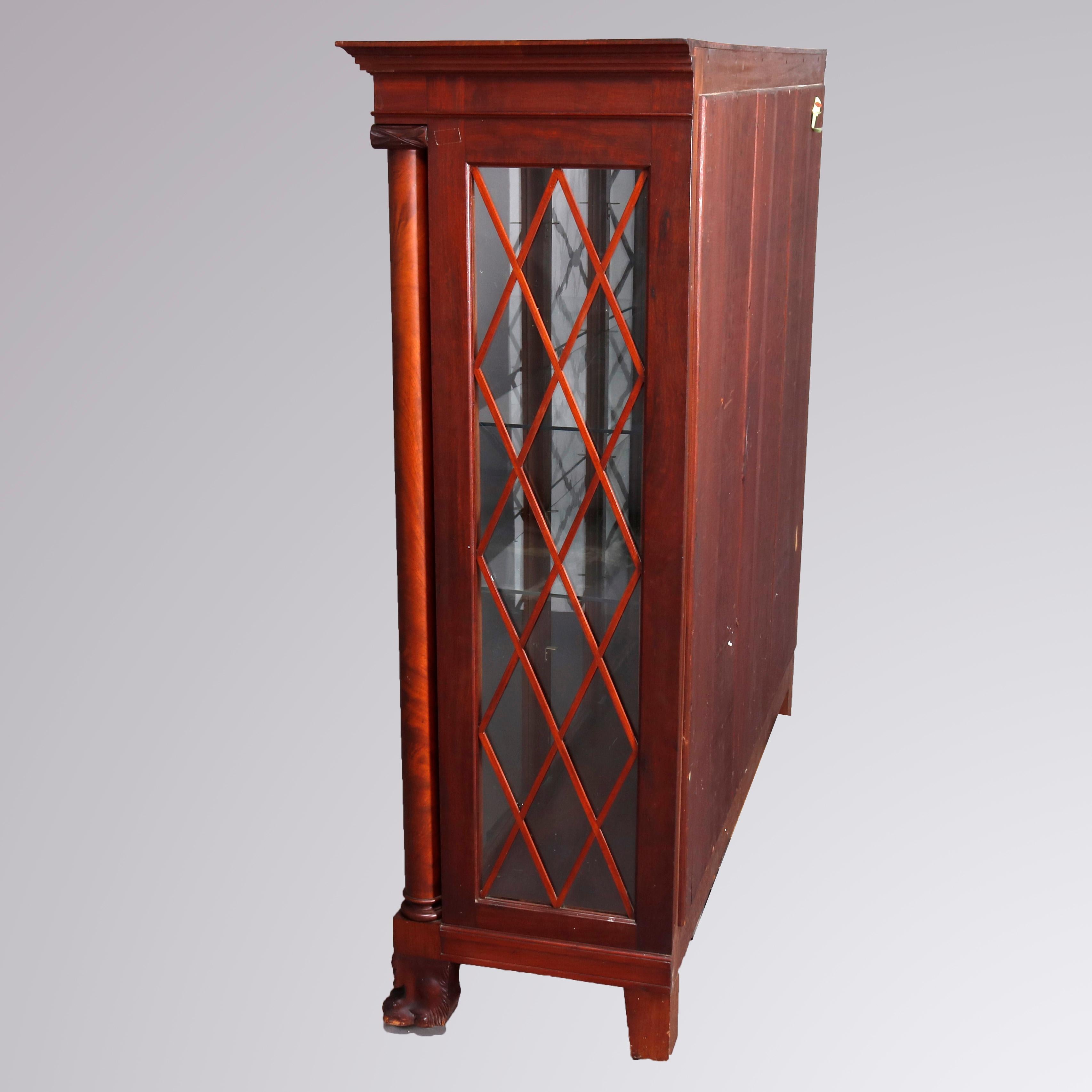 An antique American Empire display case offers flame mahogany framed case with front having three glass doors flanked by Corinthian column supports terminating in carved paw feet, sides are mullioned, shelved interior with mirrored back, circa