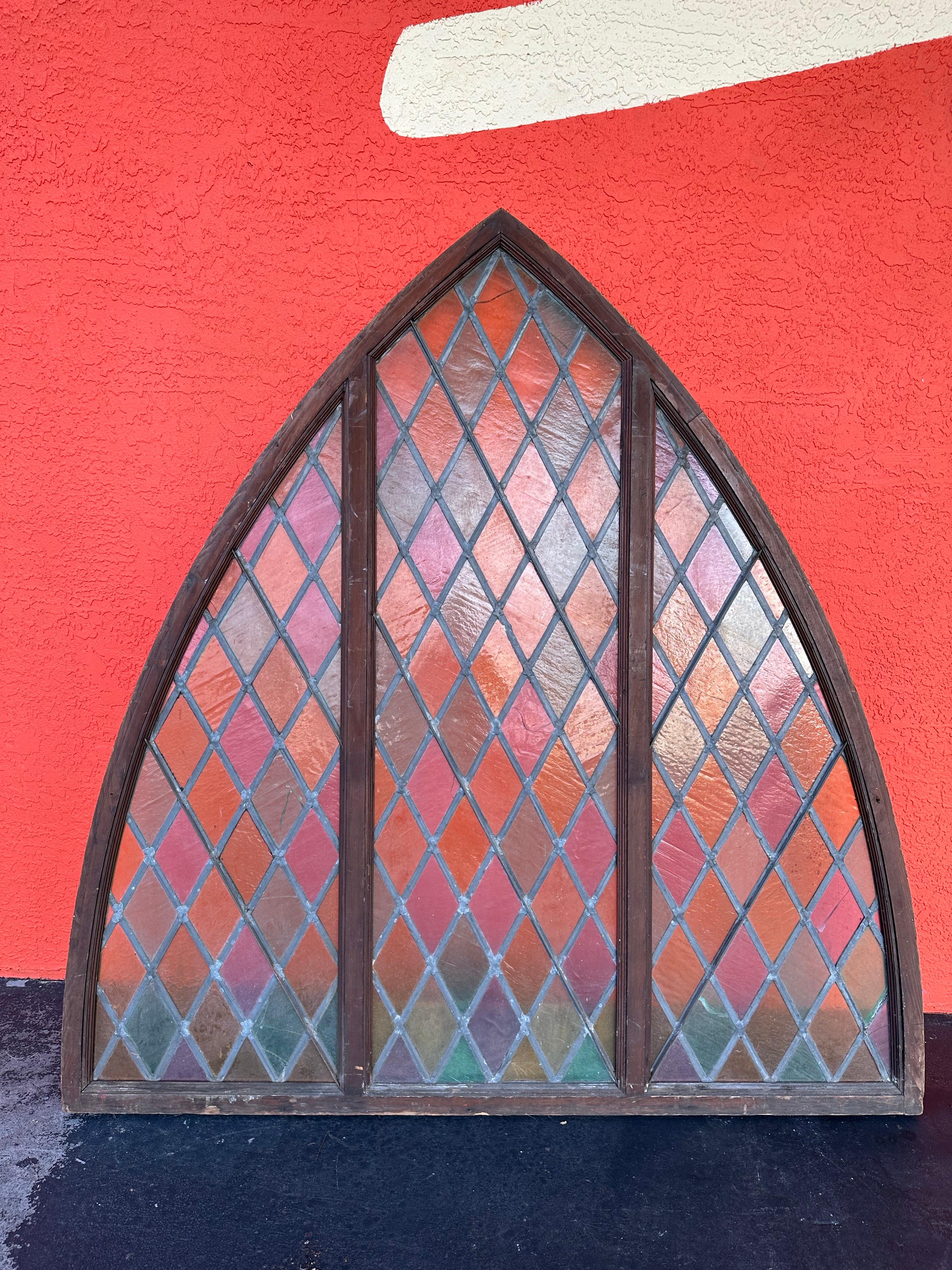 Antique Architectural Salvage Stained Glass Window. Arched shape with natural wood on one side and painted on reverse. Glass panes in green, lavender, dark yellow and light yellow. Some stress fractures to glass as shown. Wear to wood and paint as