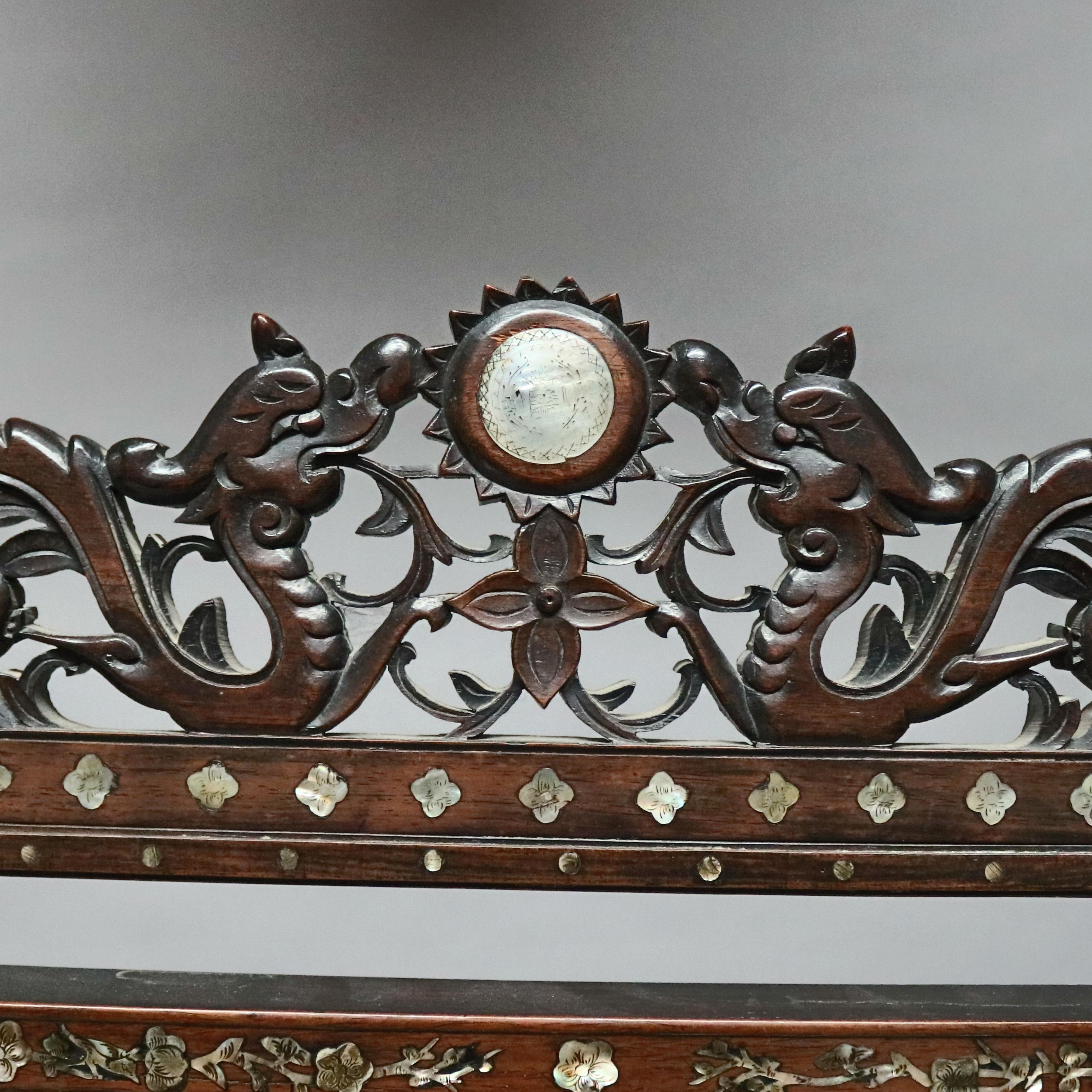 An antique and large Asian table mirror offers carved hardwood construction with dragon and foliate pierced crest surmounting frame having mother of pearl inlaid figures and flowers, swivel mirror and footed base, 20th century

Measures: 36.75