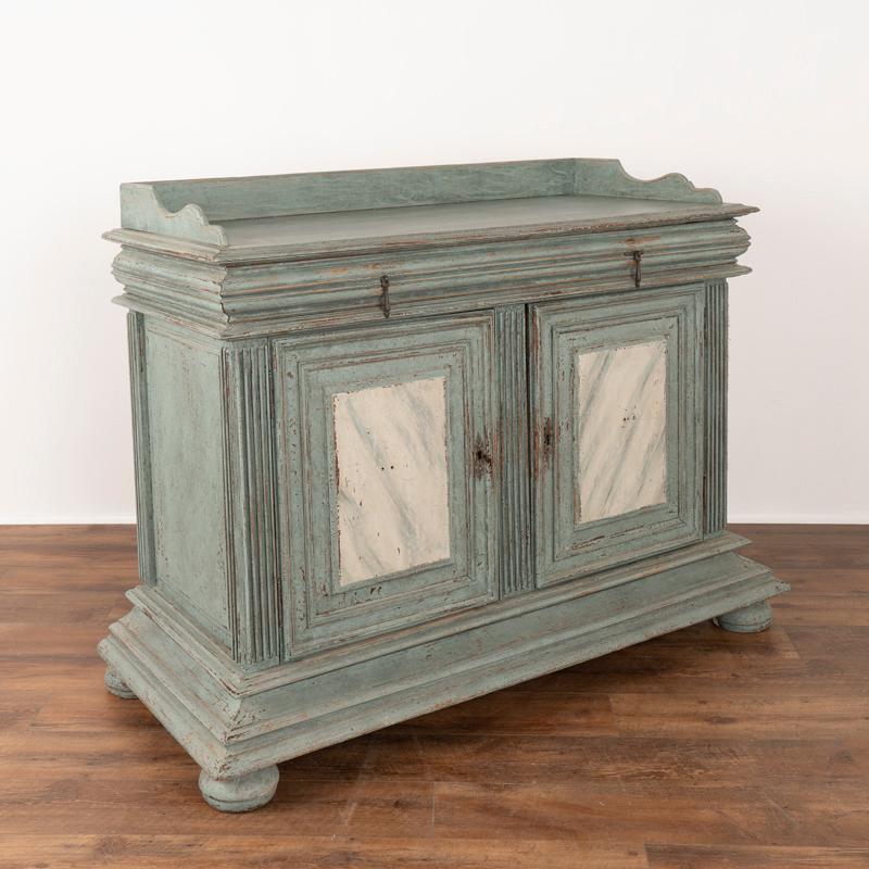 The heavily paneled doors and attractive blue painted finish draw one to this handsome oak sideboard. The newer professionally applied blue finish reveals layers of paint and distress that add an aged grace to this cabinet that was crafted in the