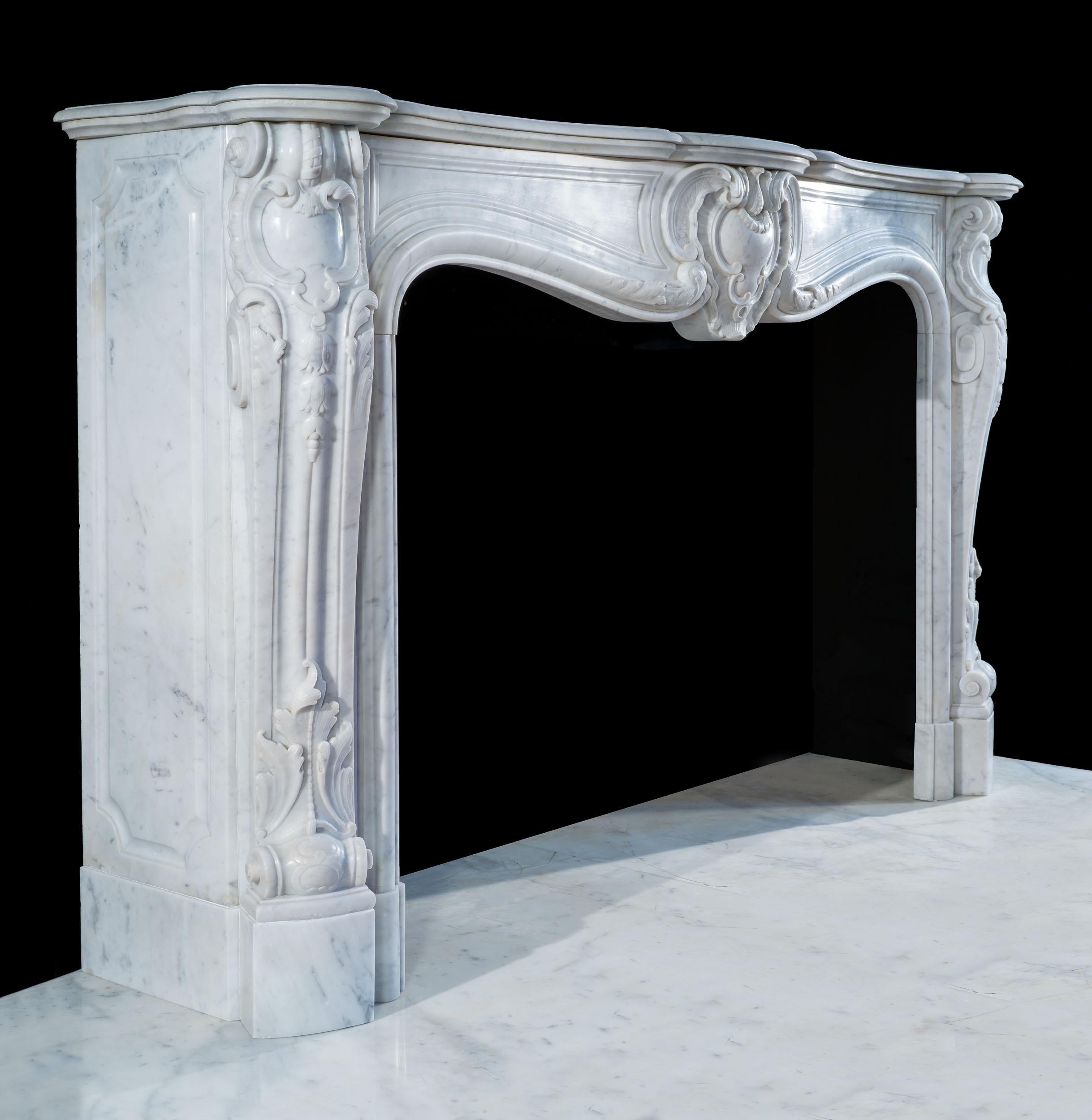 A fine French Louis XV chimneypiece in a softly mottled Carrara marble, which epitomises the Rococo style. The wide, moulded serpentine shelf rests on the boldly carved console jambs, which flank the serpentine opening, centred by a rocaille