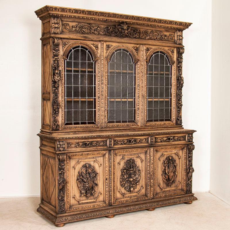 Impressive in every way, this heavily carved oak display cabinet makes a dramatic impression. The hunt cabinet motif includes birds, fish, oak leaves, grapes, nuts and more. The original lead glass arched cabinet doors are trimmed with red glass