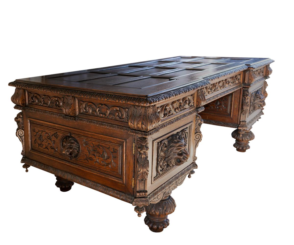 A very large and impressive carved oak baronial glass top desk with gilded embossed leather chair. This desk stands on four large bun legs and features lion face on doors. it has a two door cabinet with pull out tray and original working lock and