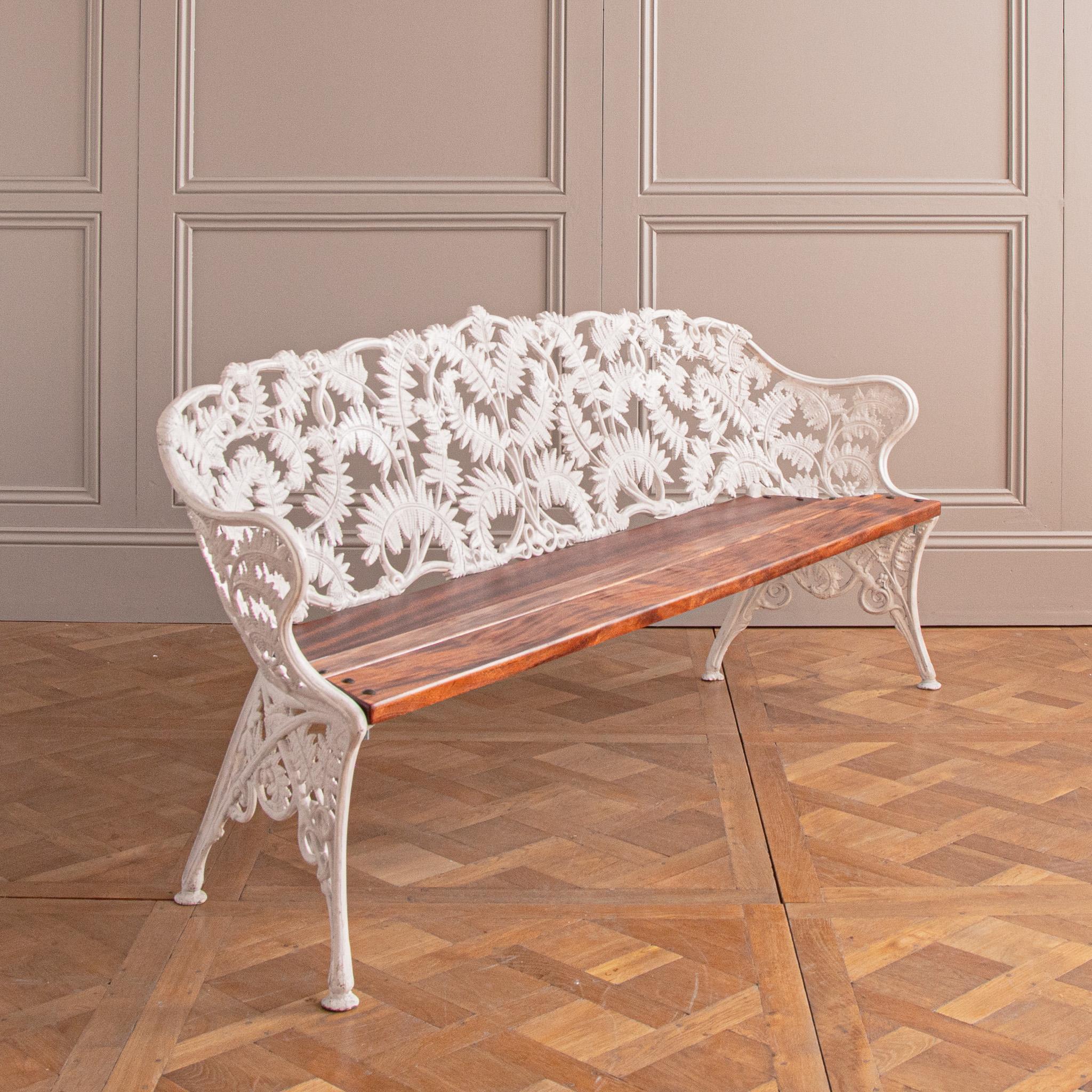 A generously large, antique garden bench, circa 1920, which seats up to 4 people comfortably. The bench is made in cast iron, white painted, that has a design featuring intertwined and beautifully animated fern motifs for the body of the whole