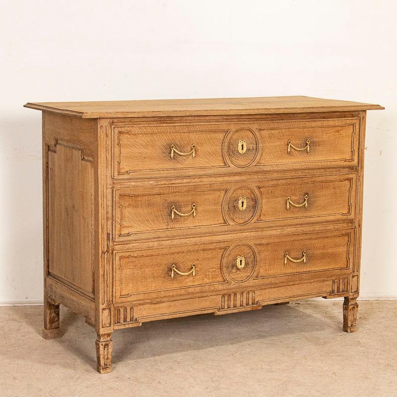This classic French oak chest of drawers has been given new life with a bleached finish which has lightened the dark oak and brings out the lovely carved details of the paneled drawers, sides and feet. The swag shaped double brass pulls accent the 3