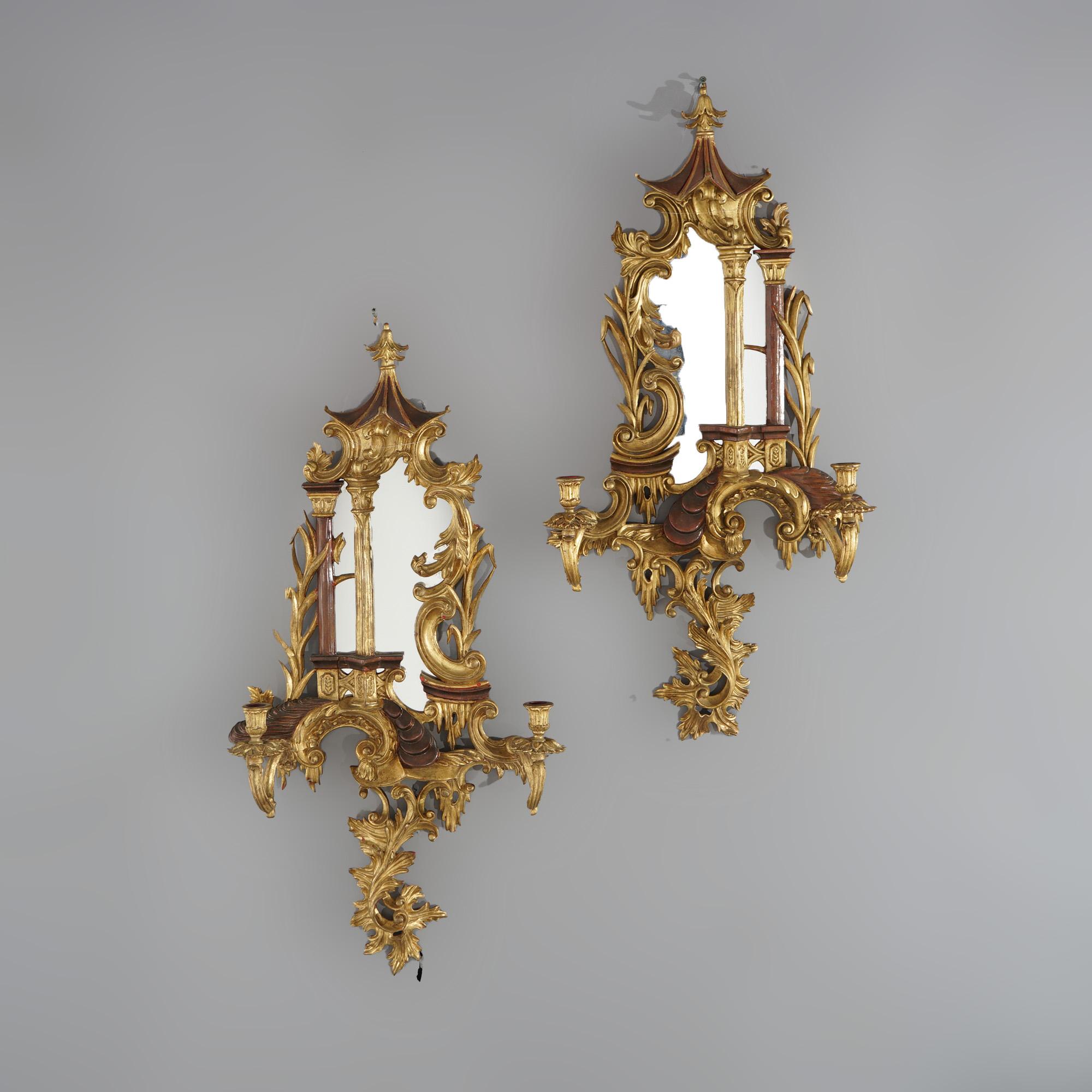 An antique pair of large English Chinese Chippendale wall sconces offer carved giltwood construction in pagoda form with polychromed finish, central mirror, foliate elements throughout and double scroll form arms terminating in candle sockets,