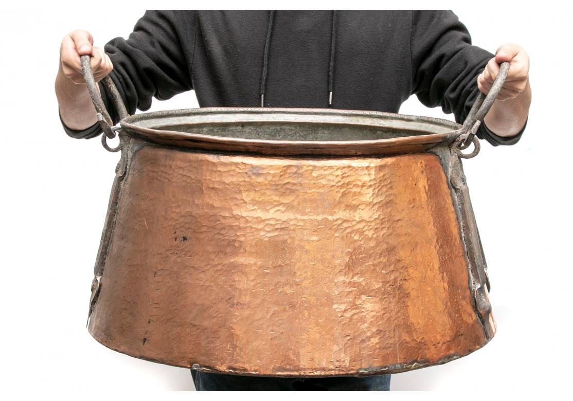 A deep hand hammered copper cauldron with twin iron handles and long pointed mounts. 
Dimensions: 22