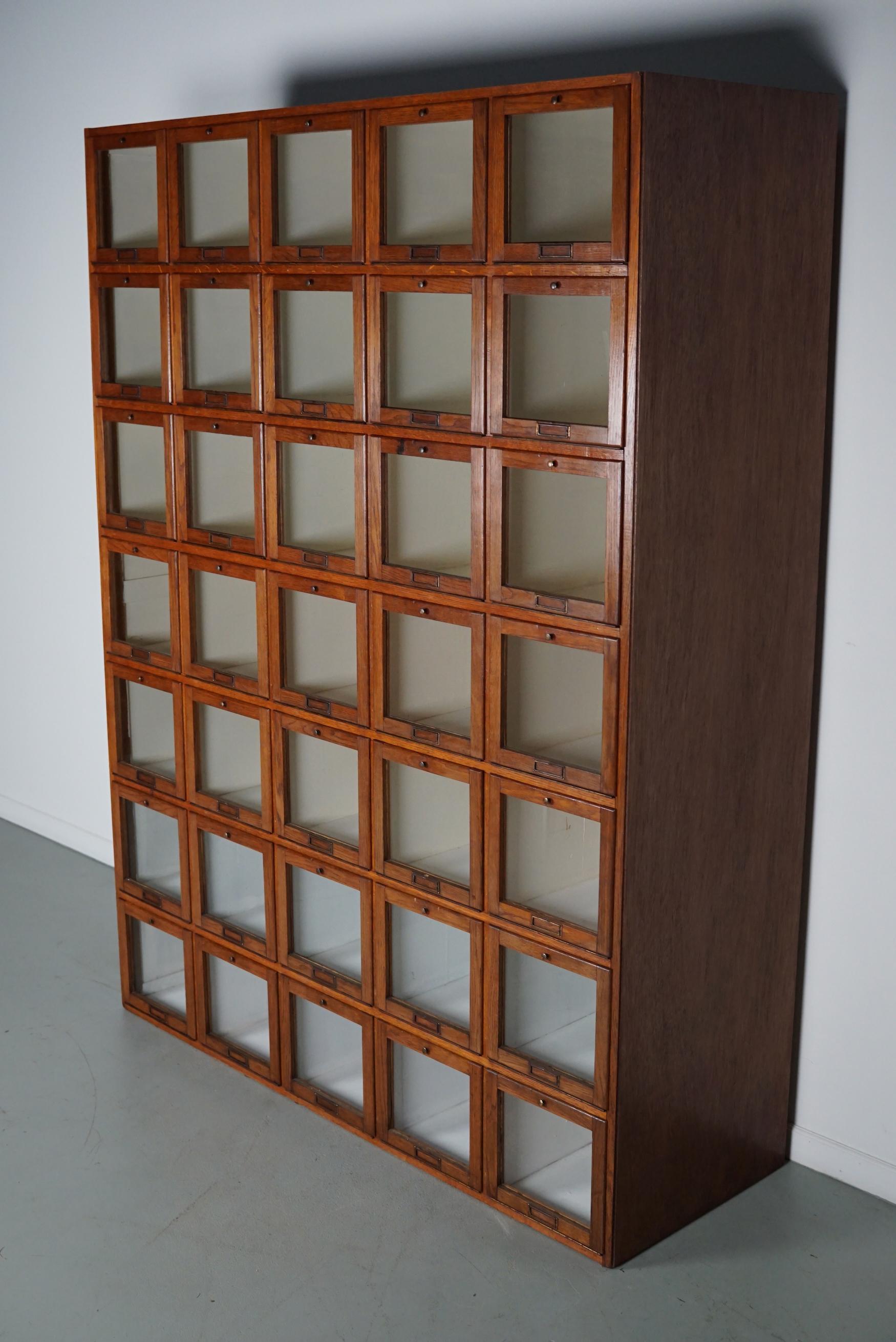 This very unique haberdashery cabinet was produced during the 1920/30s in the Netherlands and used in a shop for mens clothing. It features 35 compartments with glass fronts / folding doors and brass hardware. The interior dimensions of the