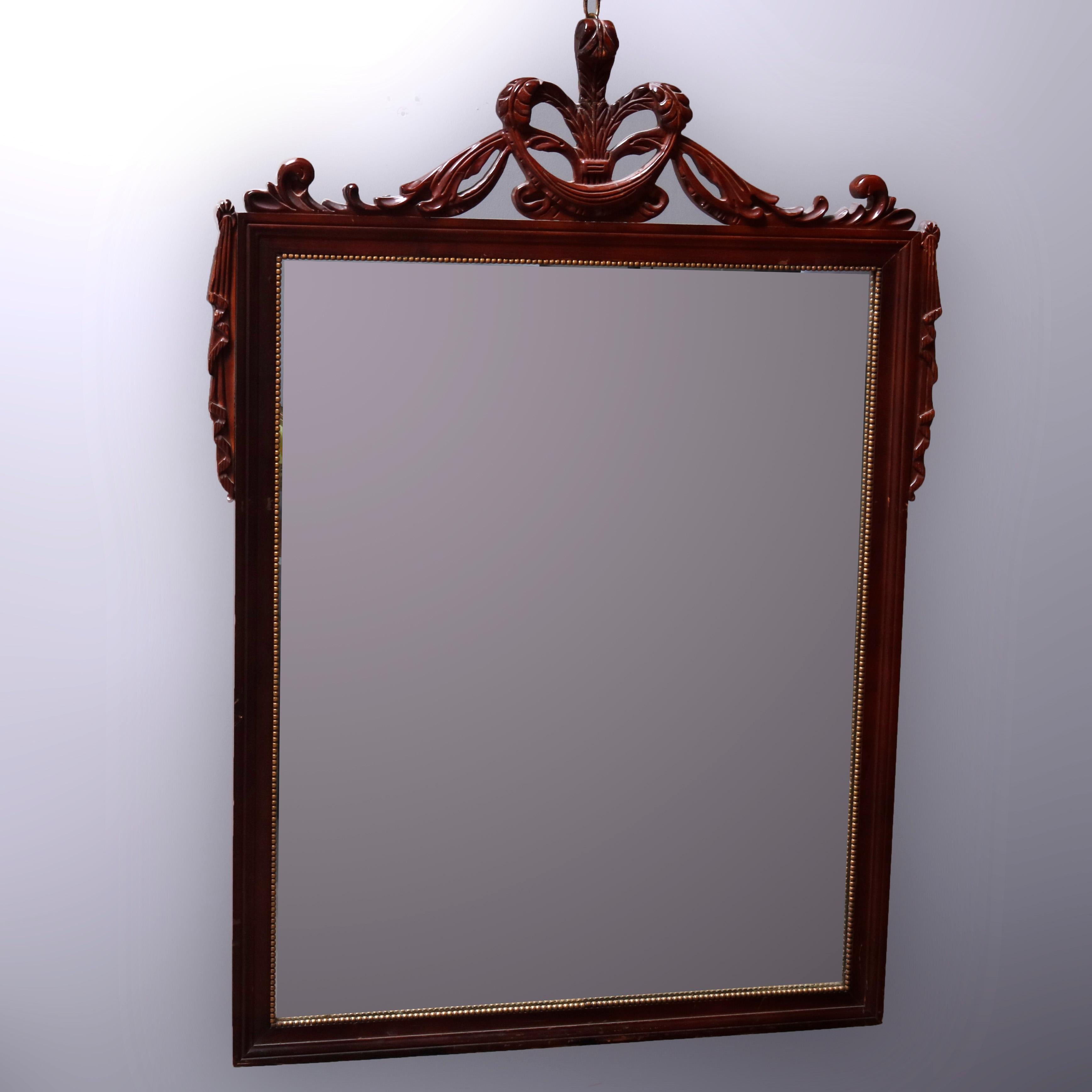 An antique Classical French wall mirror offers carved mahogany frame with pierced palmette fleur de lis crest with flanking draped garland and foliate elements, frame interior with gilt bead bordering, circa 1930

***DELIVERY NOTICE – Due to