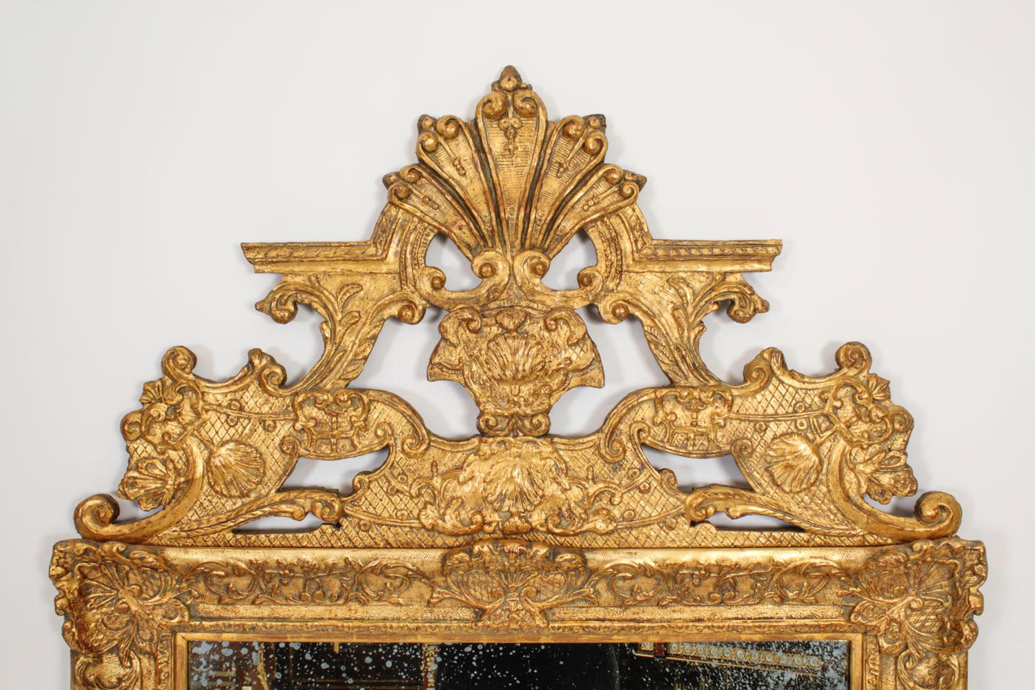 Il s'agit d'un grand et impressionnant miroir mural en bois doré et gesso sculpté de style Louis XIV, datant de 1760 environ.

Le cadre est surmonté d'un fleuron central en bois doré, sculpté et ajouré, avec un décor de coquillages, de feuilles