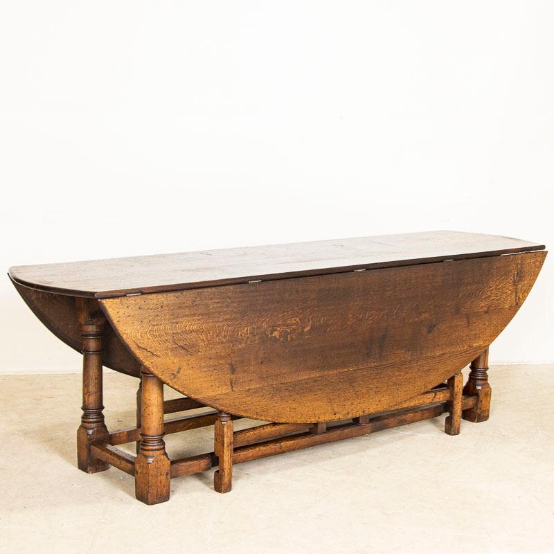 This handsome gateleg dining table is also known as an English wake table with drop leaves. Notice the dark patina of the oak, aged and naturally distressed over generations of use and lovely turned legs. The large oval shaped top has 2 drop leaves,