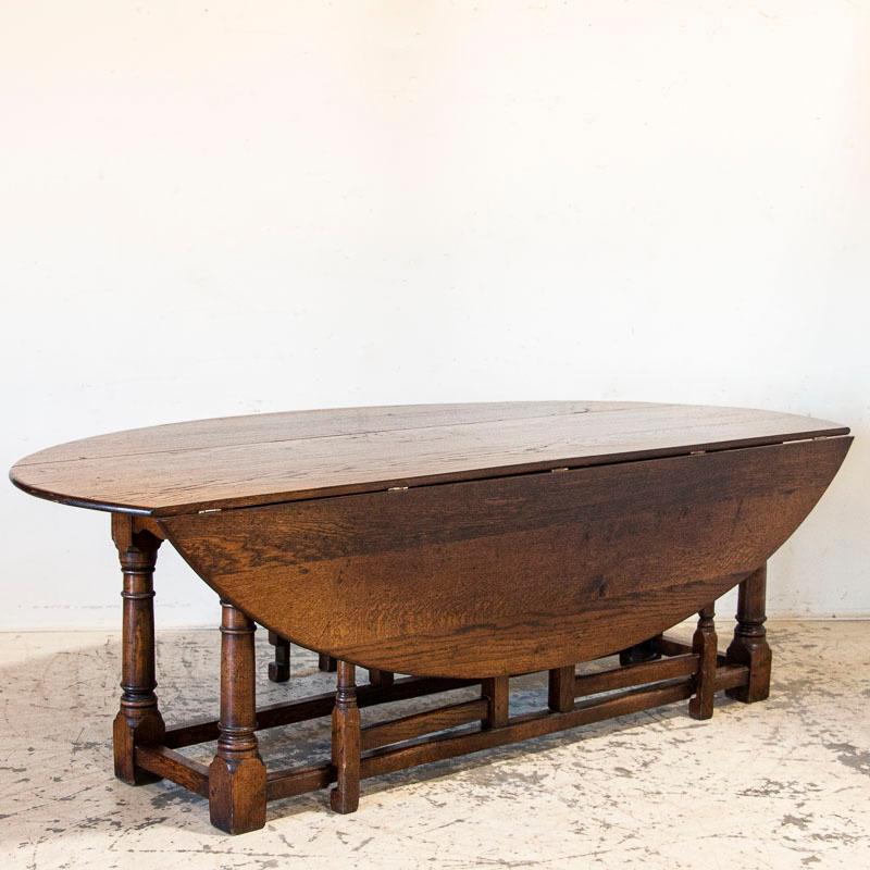 This striking drop-leaf dining table is also known as an English wake table. Notice the deep patina of the dark oak, aged and naturally distressed over generations of use. The large oval shaped top has 2 drop leaves, so when closed it serves as a