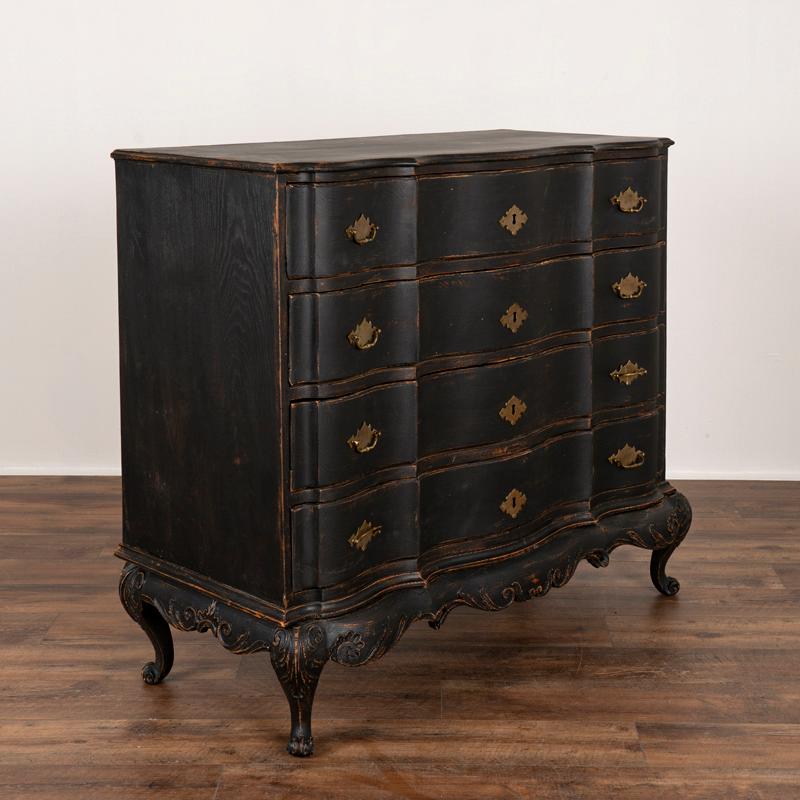 This antique rococo oak chest of drawers from Denmark features a serpentine front, brass hardware pulls and an exceptional (newer) matte black painted finish. Lovely carved details accentuate the skirt and cabriolet legs.  The lightly scraped off