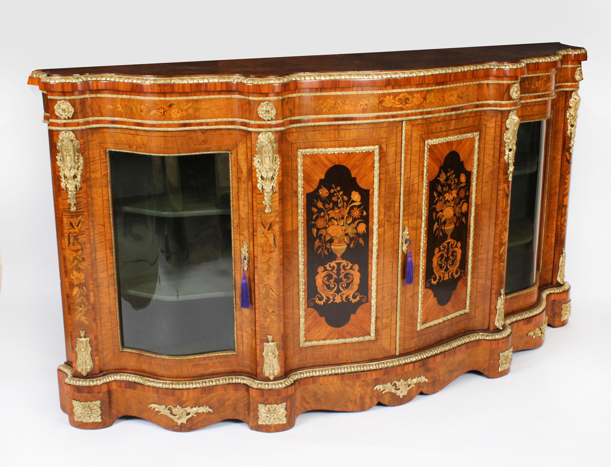 This is a superb antique Victorian ormolu mounted burr walnut floral marquetry inlaid credenza, circa 1860 in date.

The shaped top above a pair of panel doors inlaid with flowers and urns, flanked by glazed doors with shelf interior and raised on a
