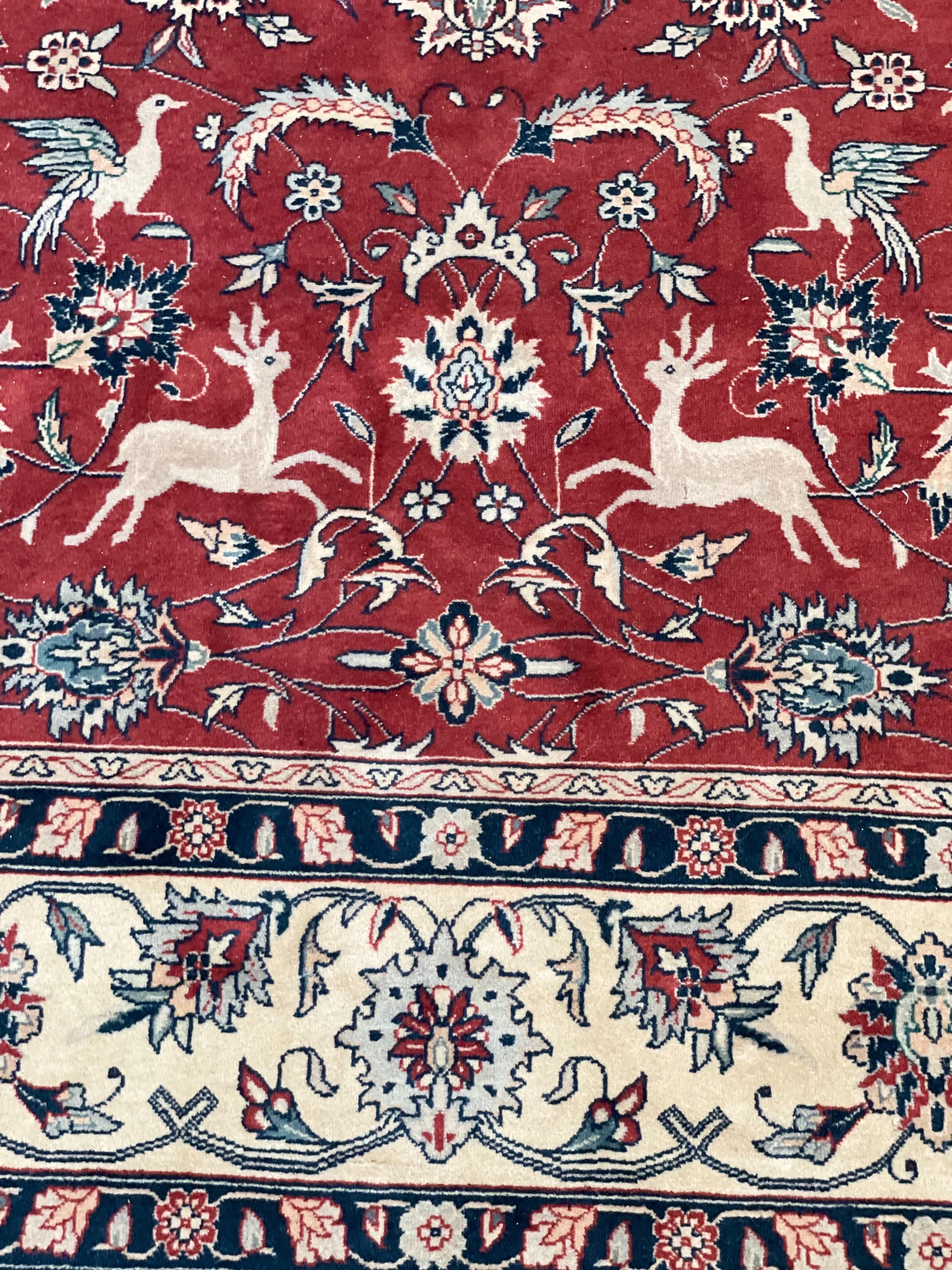 A large Persian pure-wool rug, featuring a central panel intricately woven with birds, deer and foliage, all set against a brick-red background.