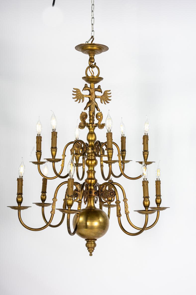 This is a fine antique brass chandelier in the traditional Dutch style, designed with two tiers of six arms each, creating an impressive twelve-light arrangement. The piece is crafted in heavy cast and turned brass, giving it both presence and