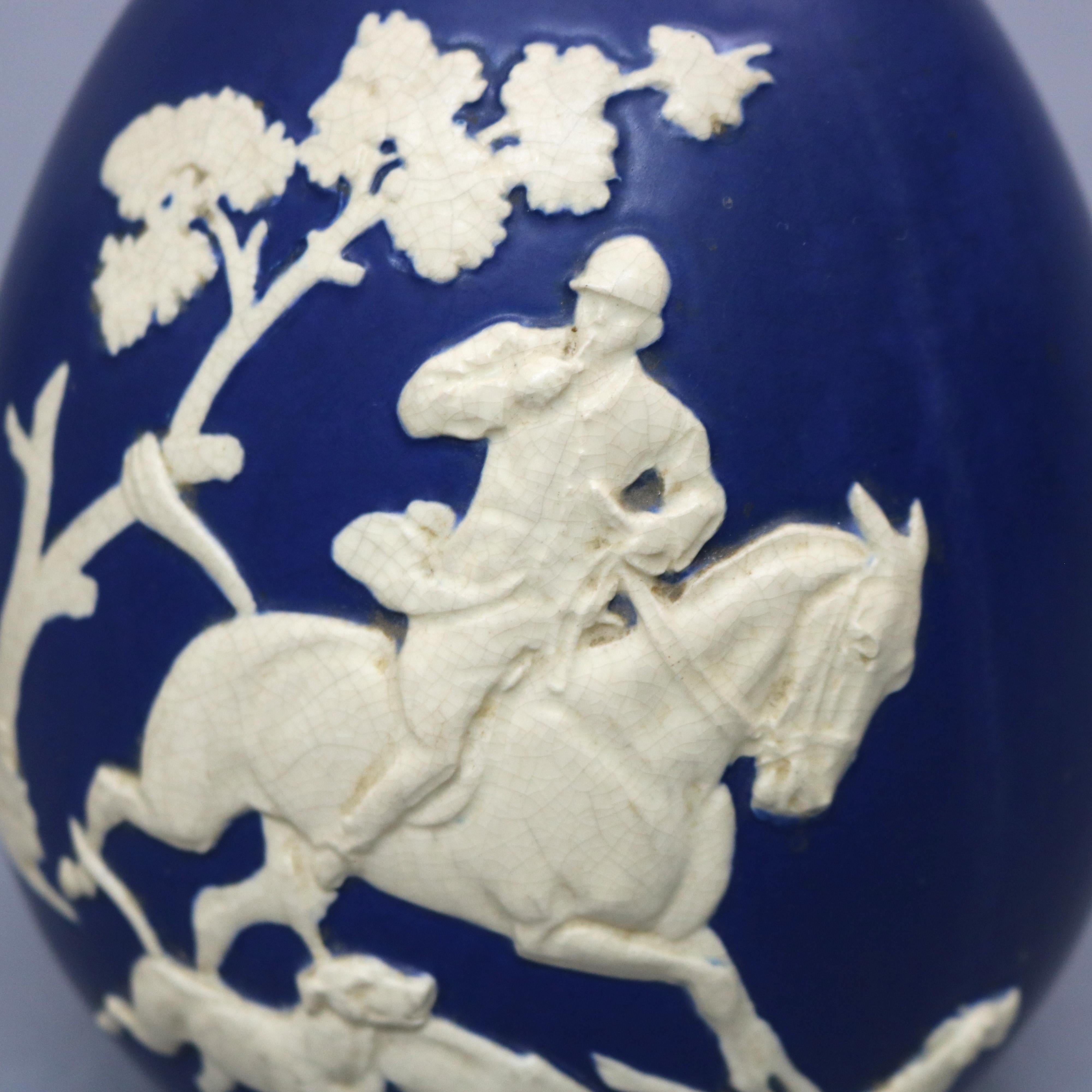 An antique and large vase by Weller offers art pottery jasperware with blue vase having fox hunt scene in white with dogs, horse, and rider, marked on base as photographed, circa 1930

Measures: 10.25