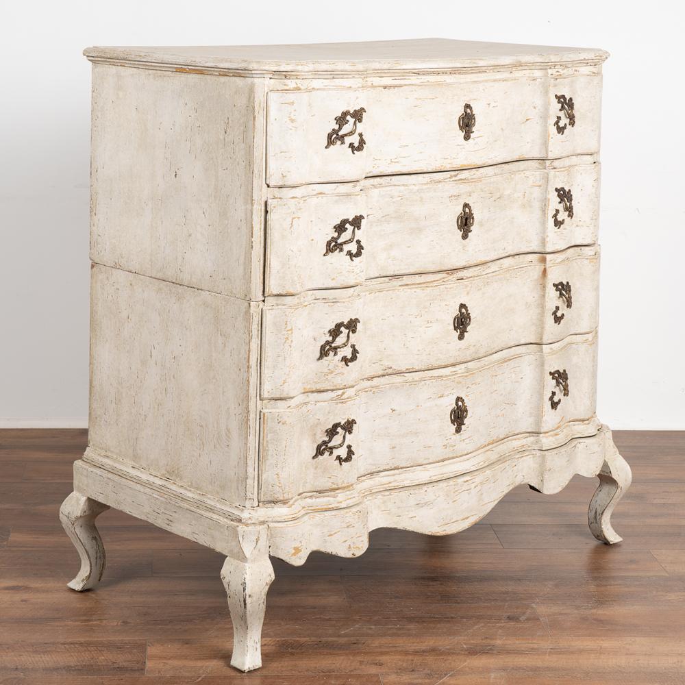The white painted finish creates the captivating allure in this attractive large baroque chest of four drawers with brass pulls.
Later professionally applied, the layers of white (with shades gray and brown undertones) paint compliment the age,